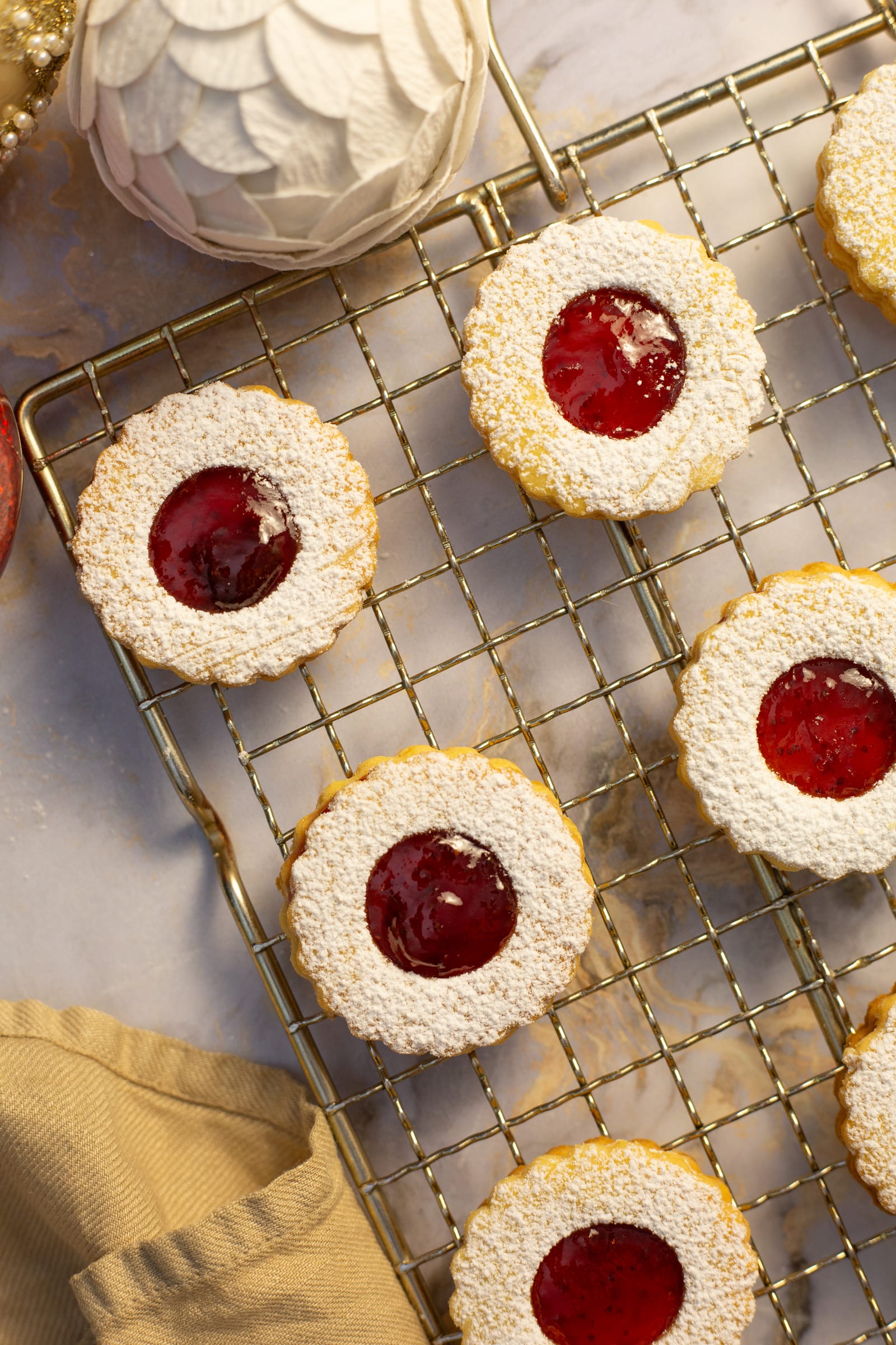 Round lemon and raspberry Linzer cookies on a wire rack beside a white Christmas bauble