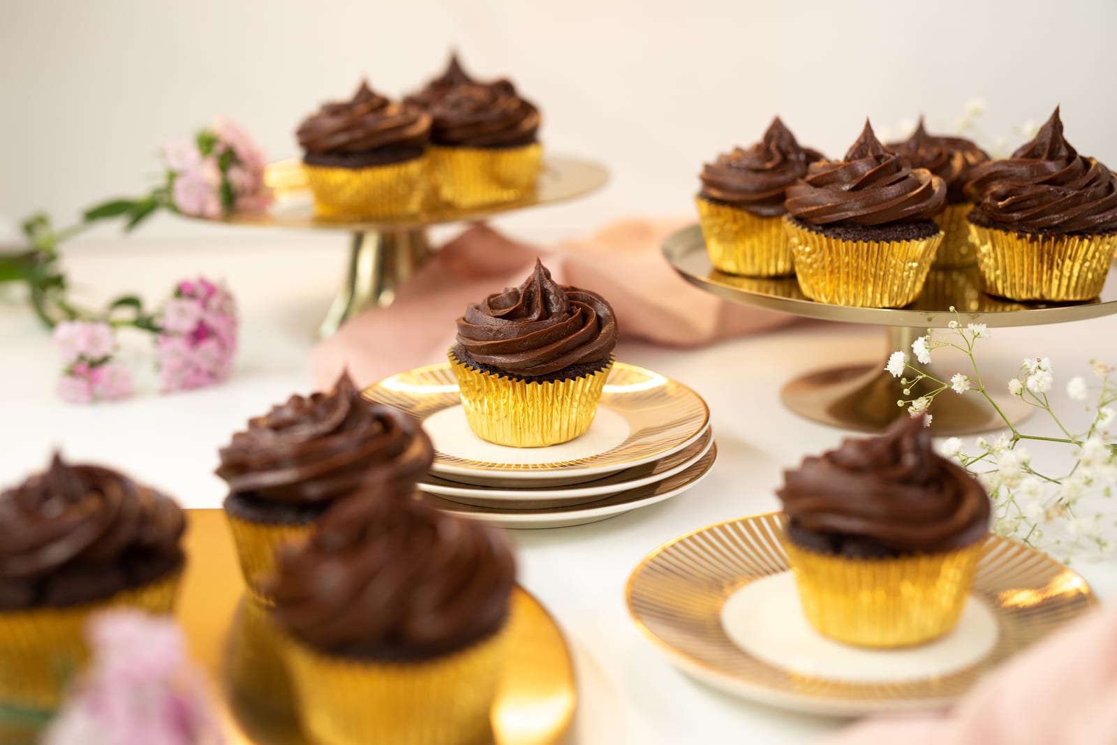 Ultimate triple chocolate cupcakes on gold plates and stands with pink flowers and a pink cloth