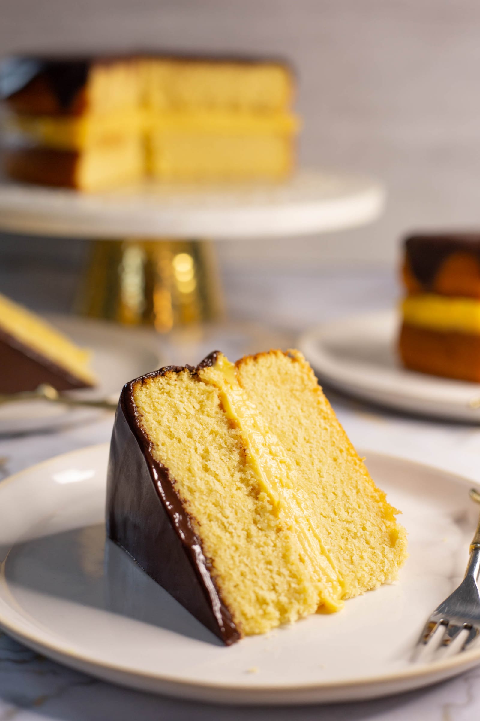 A slice of Boston cream pie with a fork, showing the sponge, custard and ganache