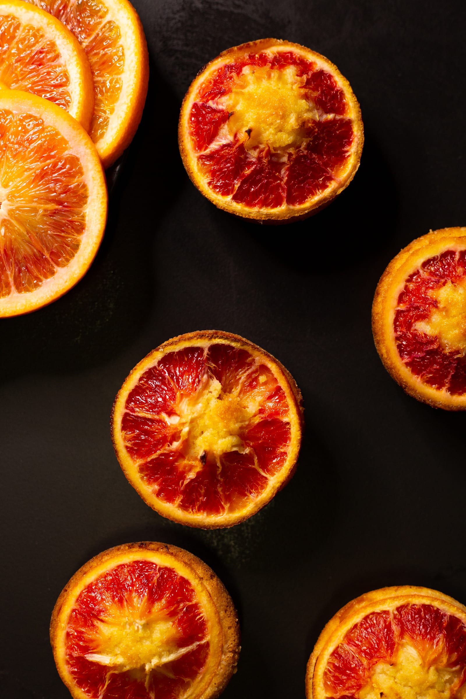Halved blood oranges on a dark surface