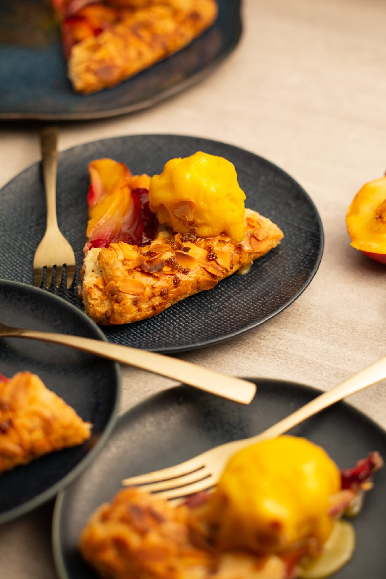 Slices of stone fruit galette with ice cream on dark plates with gold forks, from above