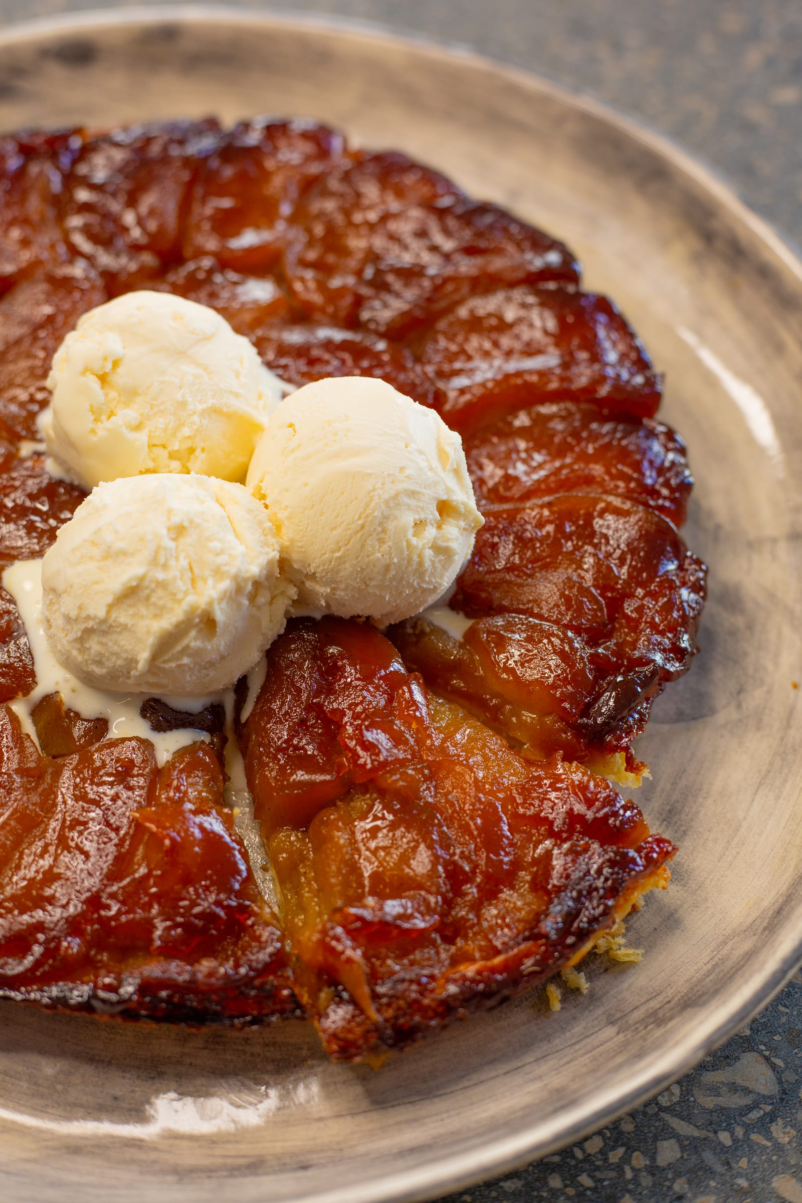 Close-up of scoops of vanilla ice cream melting on an apple tarte tatin, from above