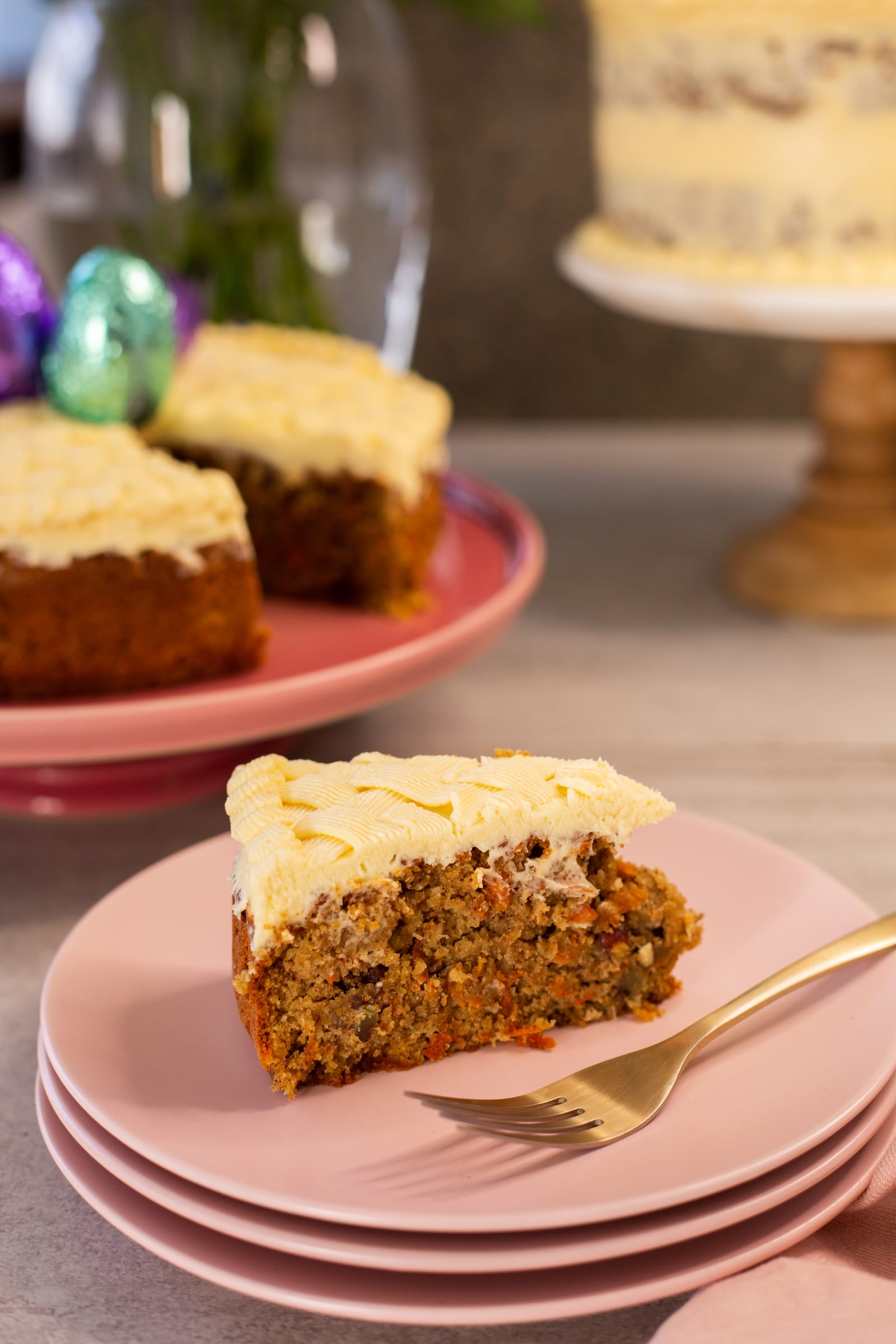 A slice of gluten-free carrot cake on stacked pink plates with a gold fork