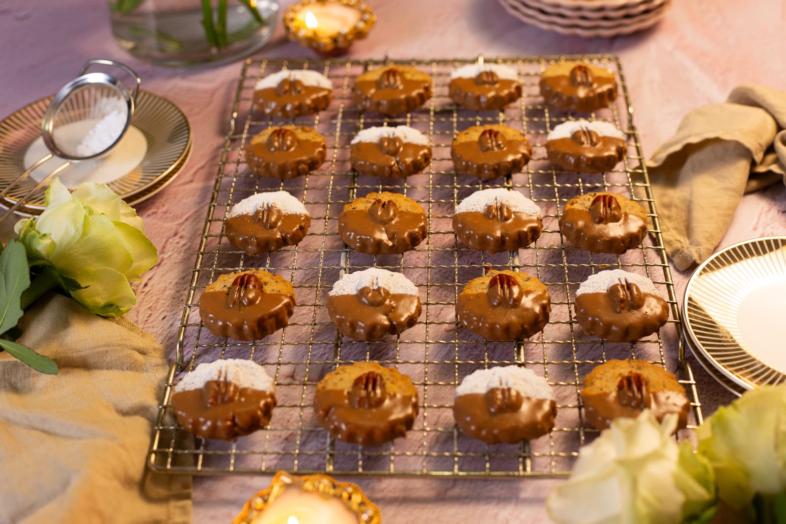Rows of pecan nut biscuits dipped in chocolate and icing sugar, on a wire rack with white roses