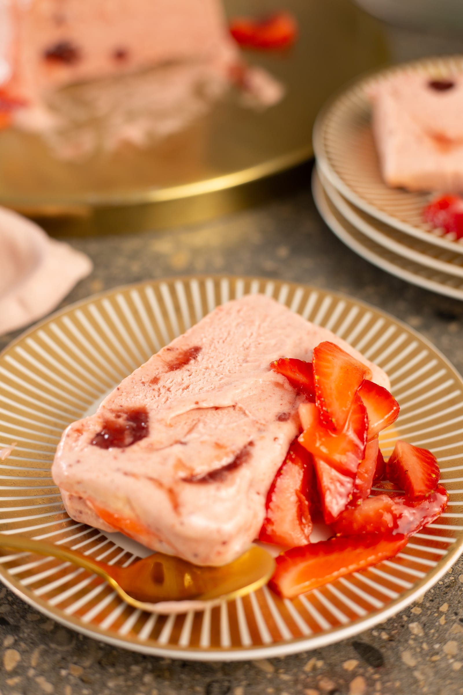 A slice of roasted strawberry and rosemary semifreddo on a gold-rimmed plate