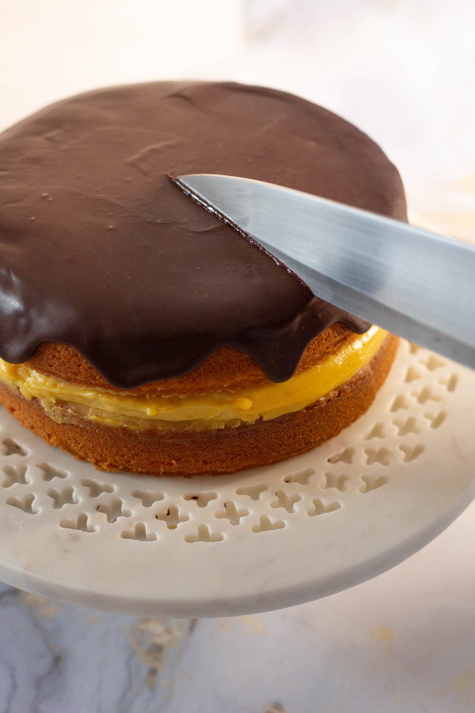 A knife cutting into the ganache-topped Boston cream pie