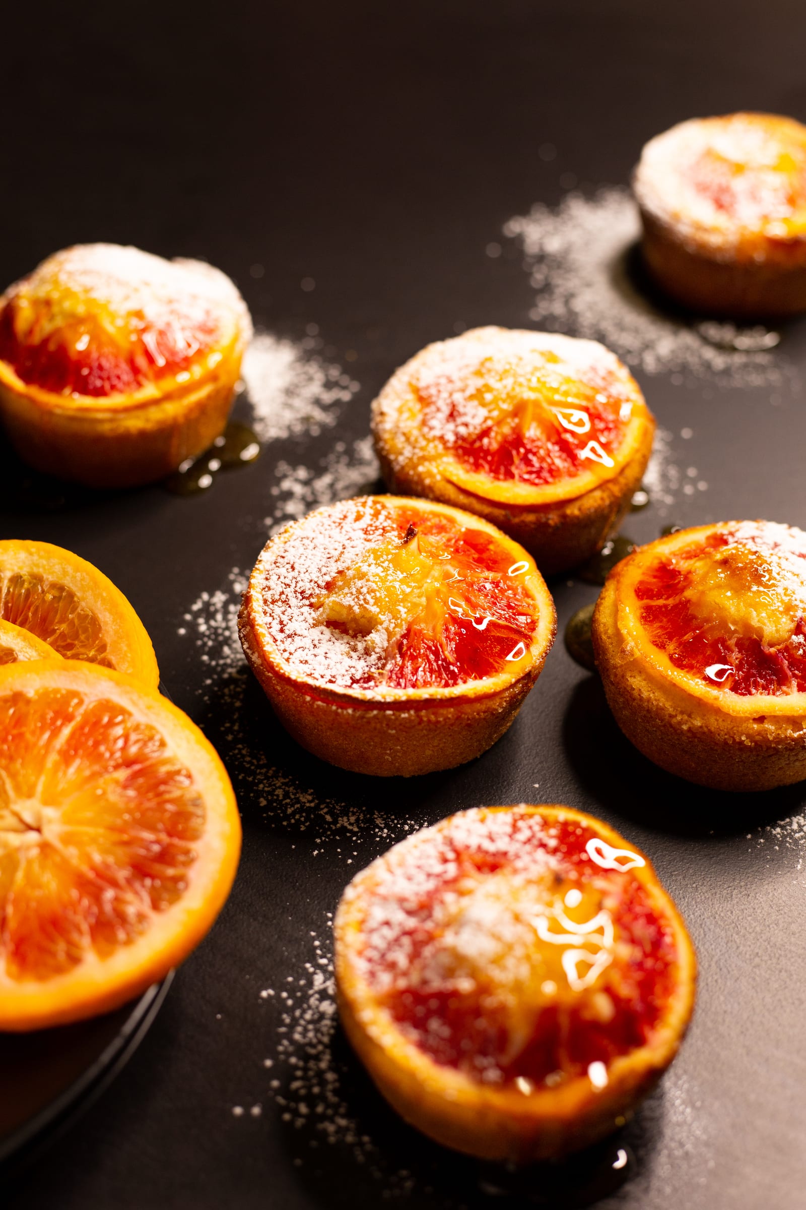 Almond, semolina and blood orange syrup cakes dusted with icing sugar on a dark surface