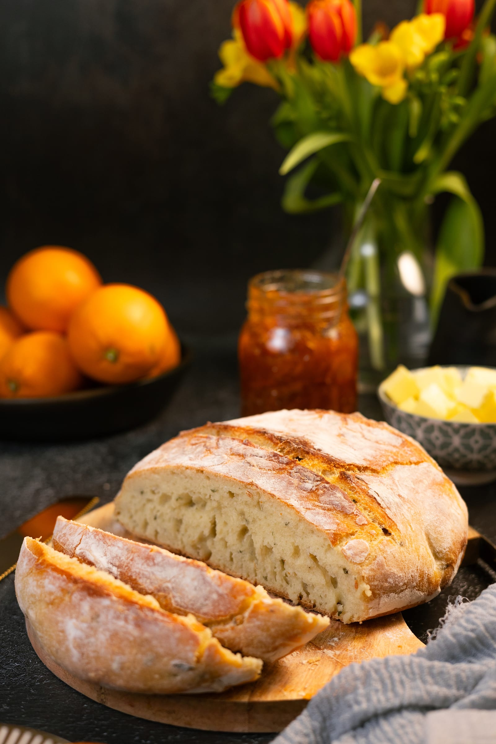 A crusty no-knead loaf, partly sliced, with oranges and marmalade behind
