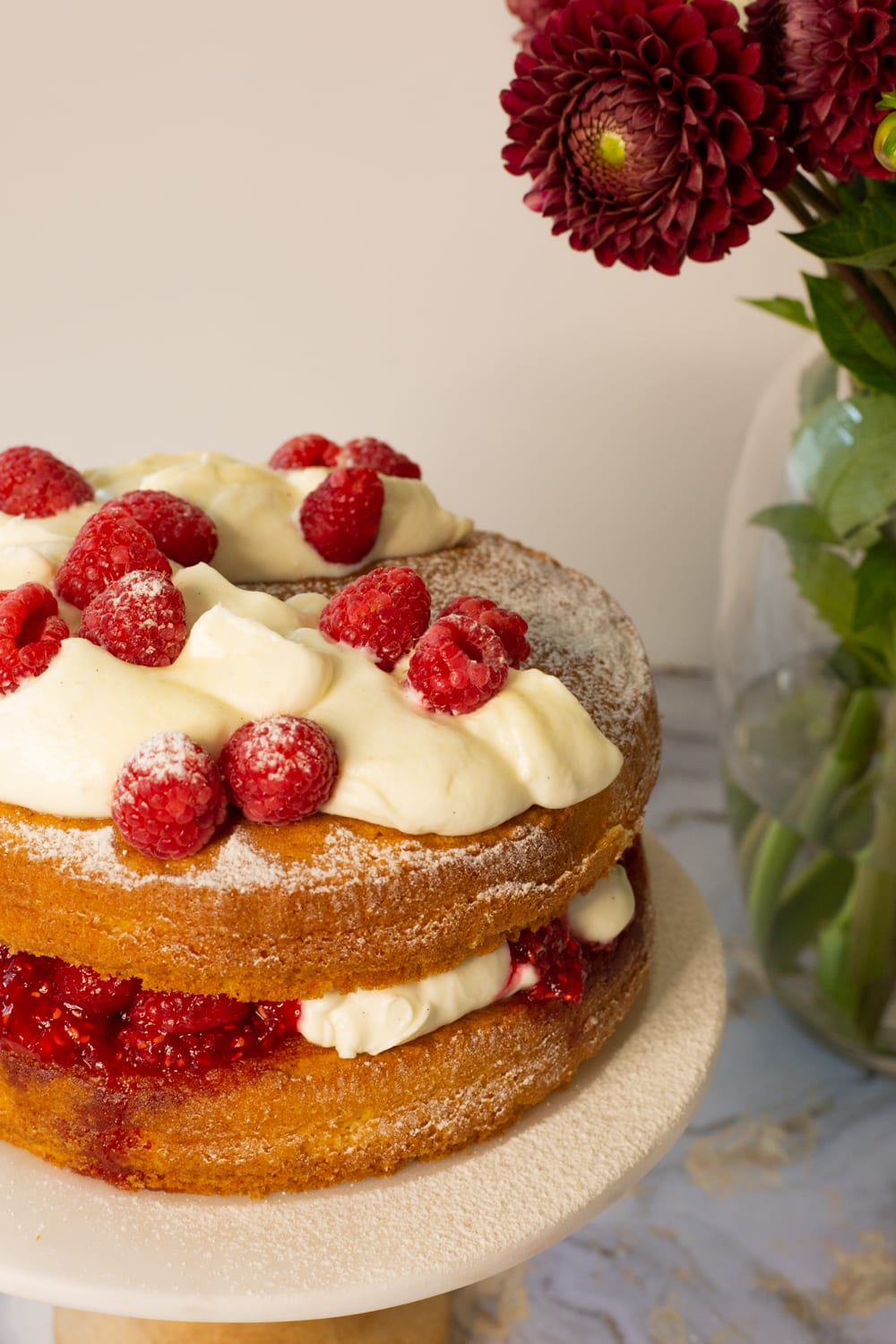 The top of a Victoria sandwich with whipped cream, fresh raspberries and a dusting of icing sugar