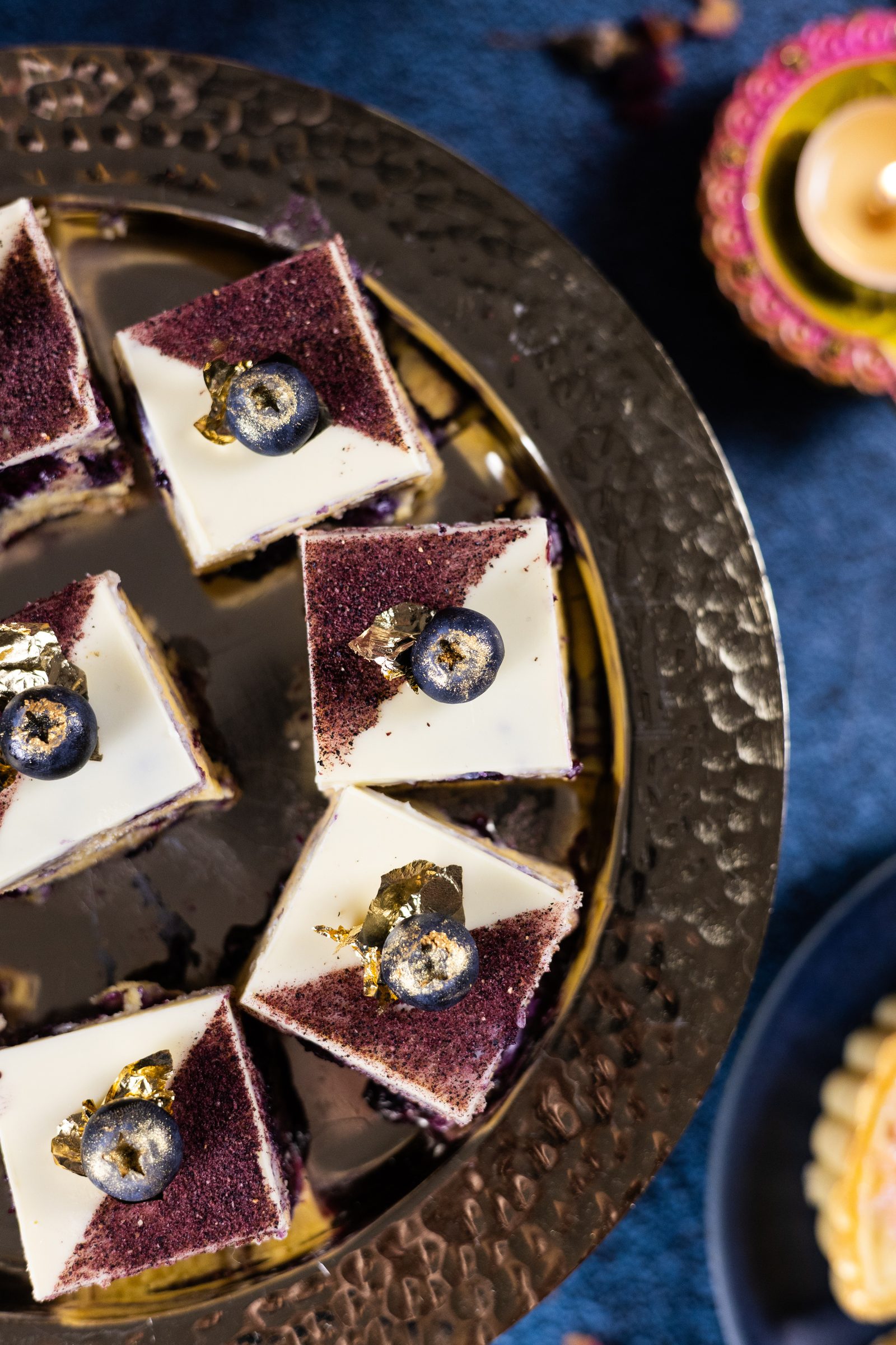 Blueberry ripple burfee squares half dusted with freeze-dried blueberry, each topped with a blueberry and gold leaf, from above