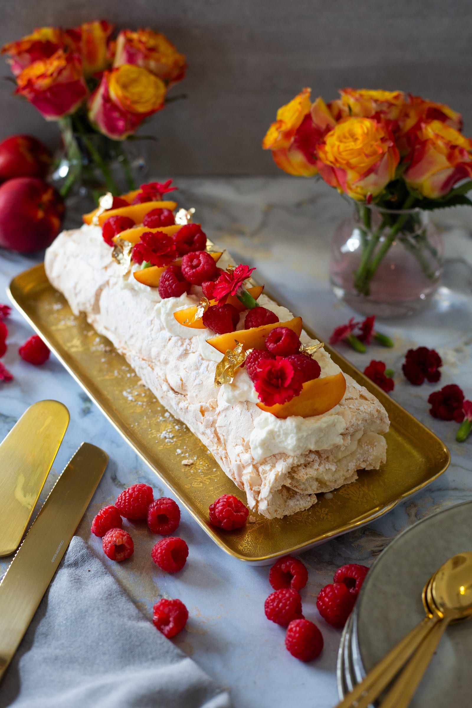A whole raspberry and nectarine pavlova roulade topped with raspberries and nectarine slices on a gold tray