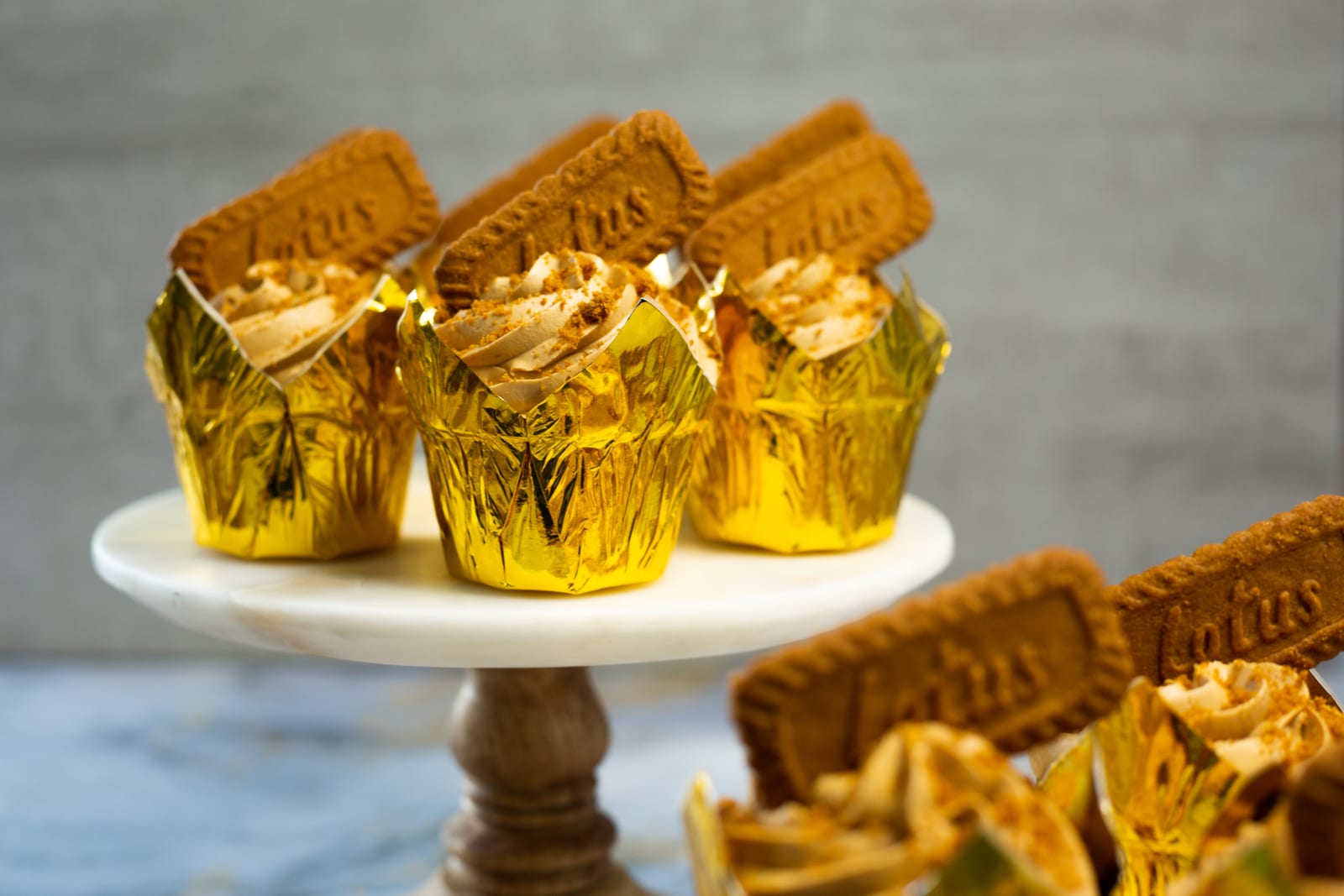 Biscoff cupcakes in gold wrappers on cake stands, each topped with a Biscoff biscuit