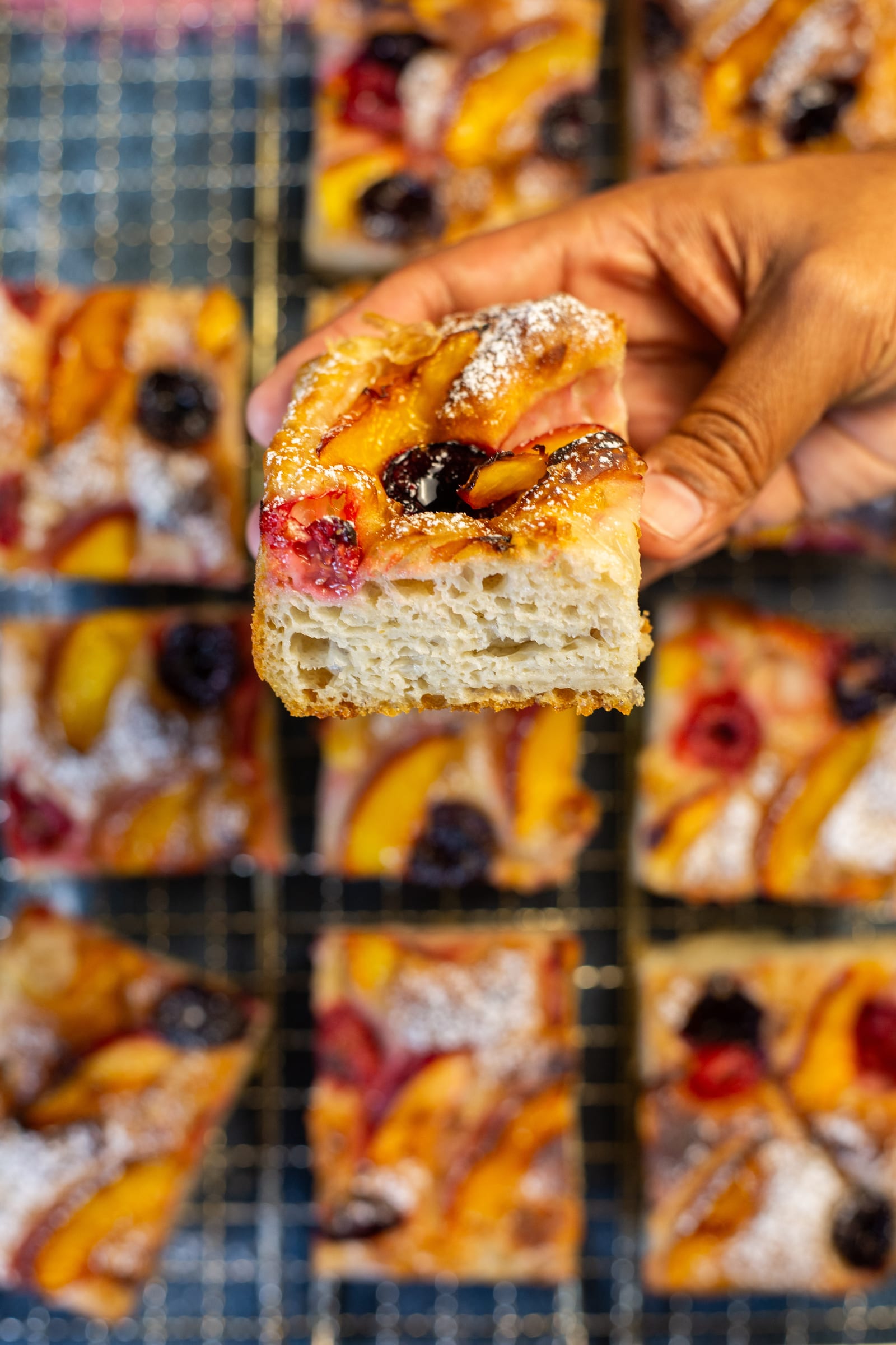 A hand lifting a square of focaccia