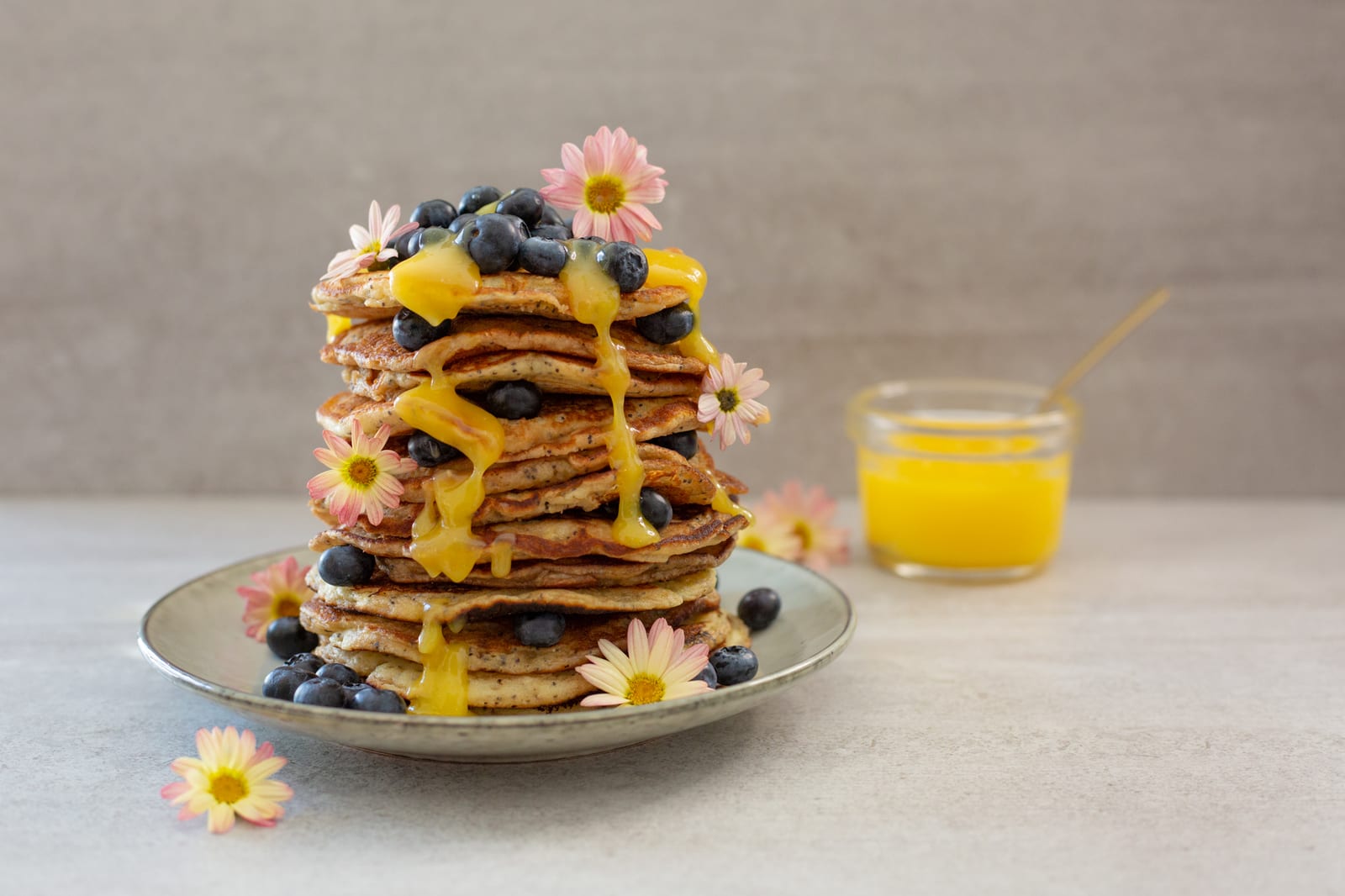 A stack of lemon and poppyseed pancakes topped with blueberries and lemon curd beside a jar of curd