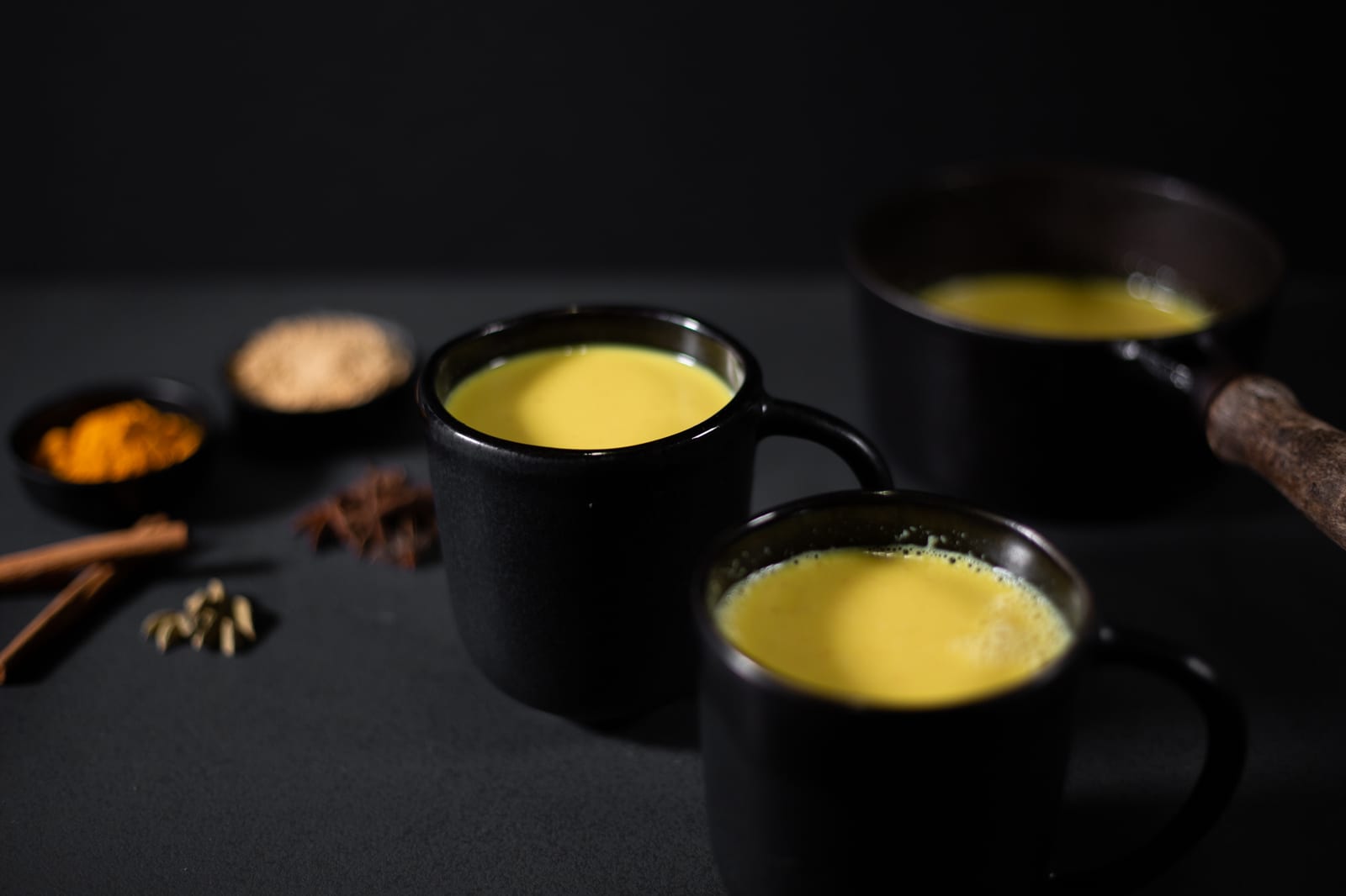 Three black mugs of turmeric and ginger white hot chocolate with cinnamon, star anise and turmeric