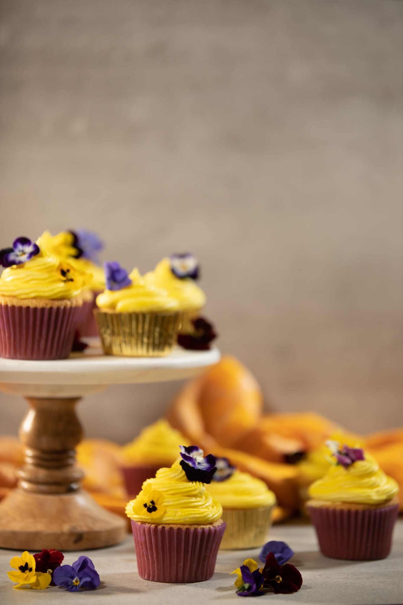 Vanilla cupcakes on and around a small cake stand