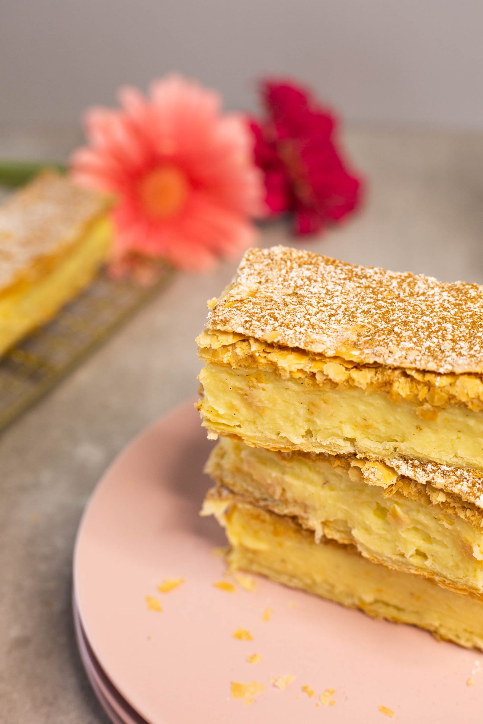 Close-up of stacked milk tart slices on pink plates, gerberas blurred behind