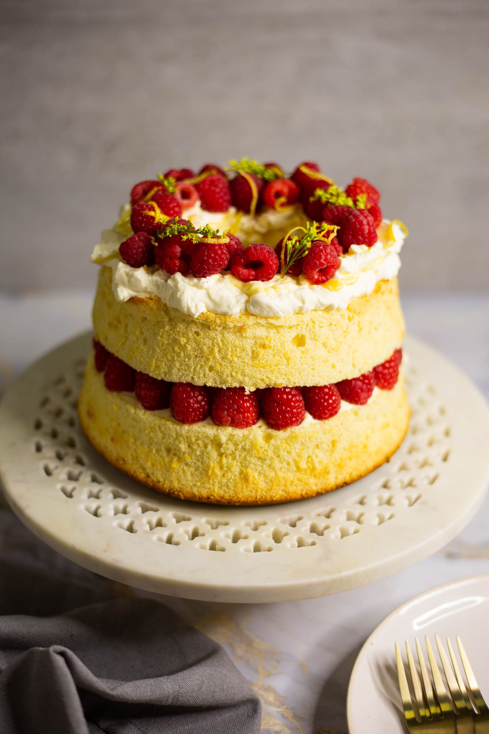 A lemon curd and raspberry chiffon cake on a white cake stand, from the side