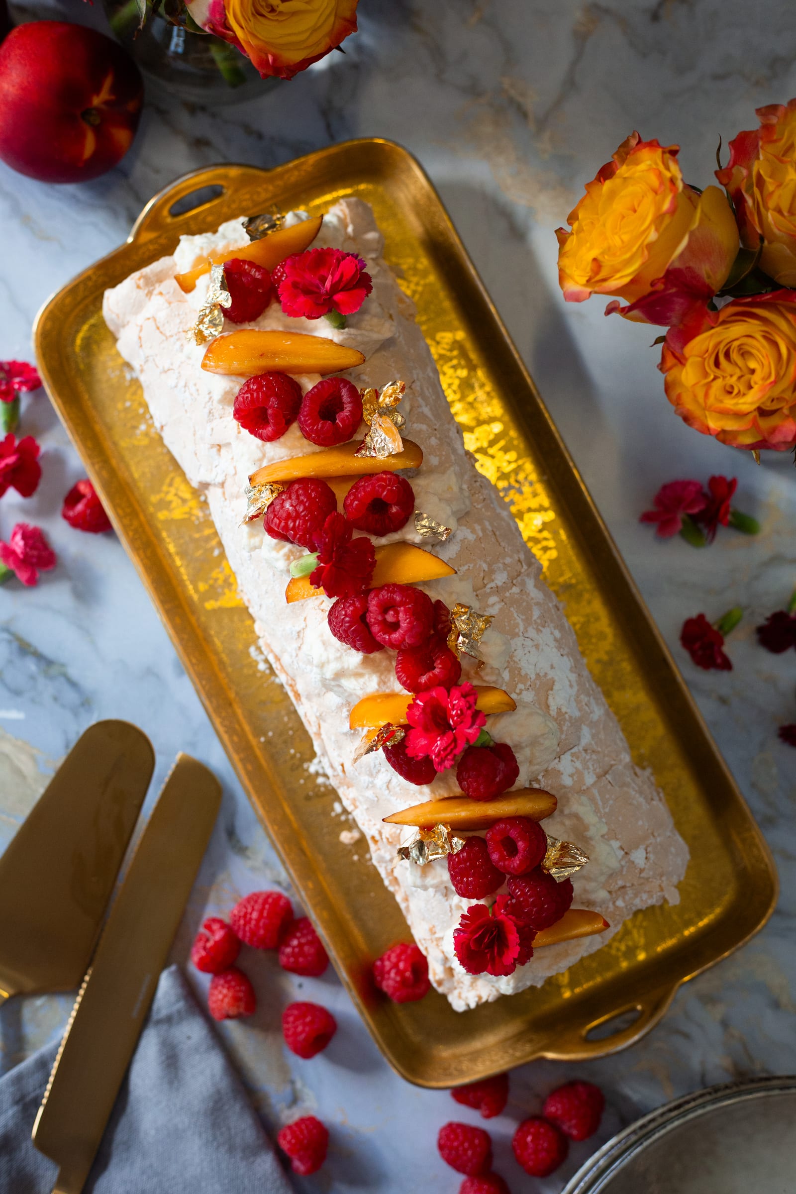 The pavlova roulade from above on its gold tray, with roses and gold cutlery