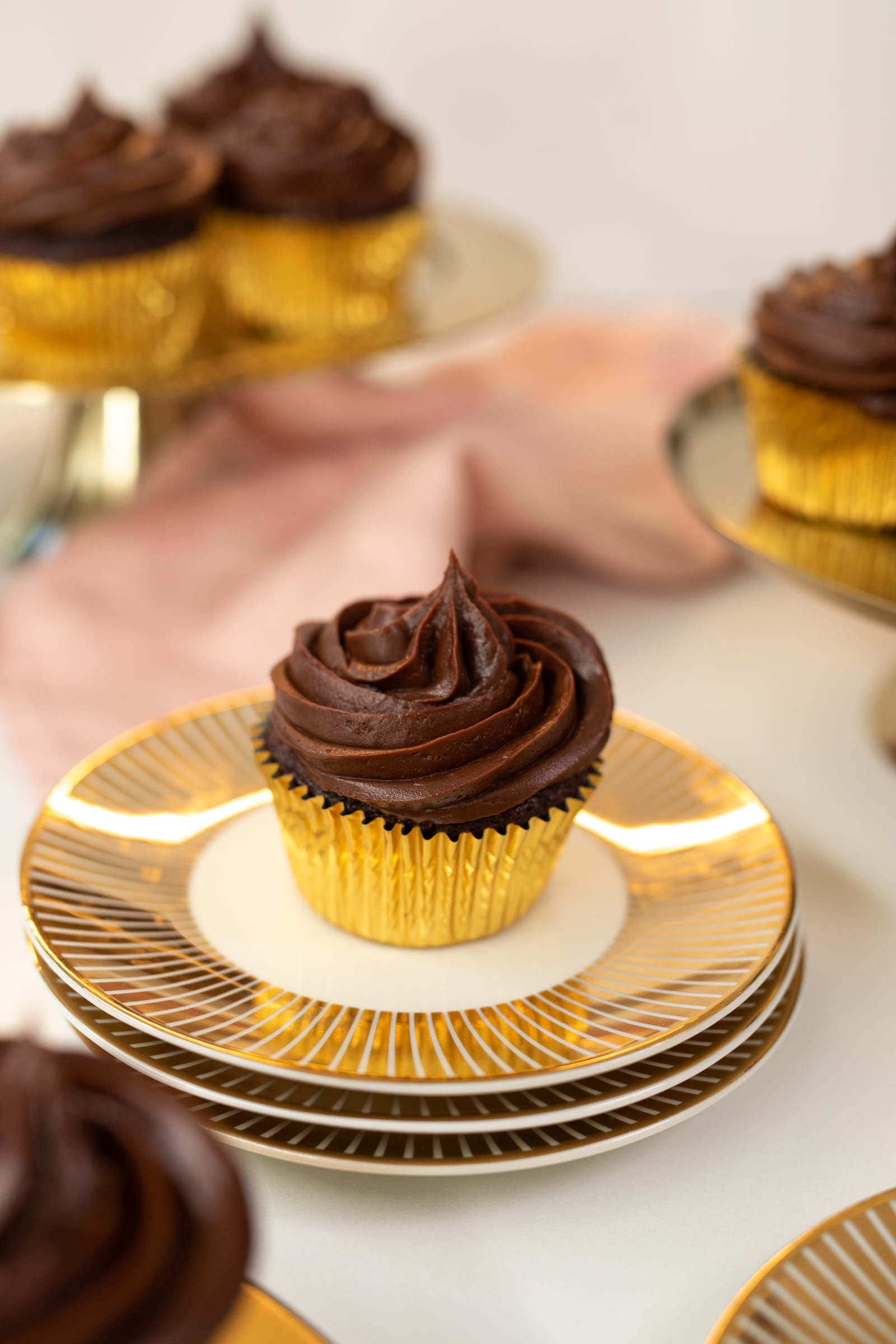 An ultimate triple chocolate cupcake on stacked gold plates with a pink cloth