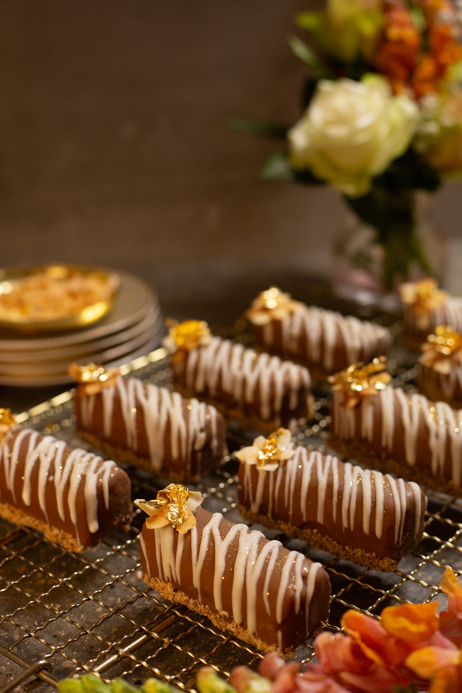 Rows of coconut, caramel and chocolate logs on a cooling rack beside a vase of roses