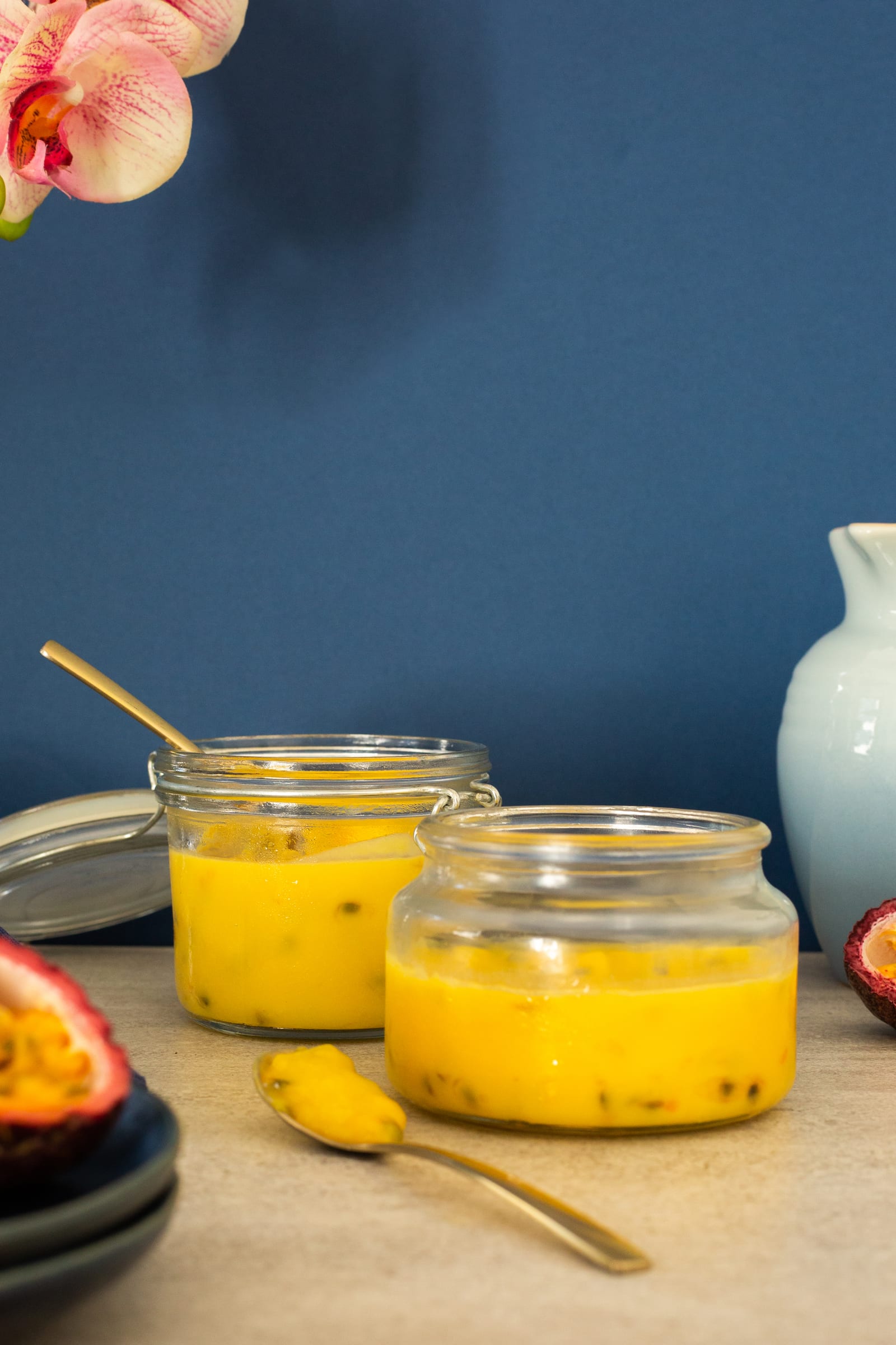 Jars of passionfruit curd with a spoonful in front and an orchid above