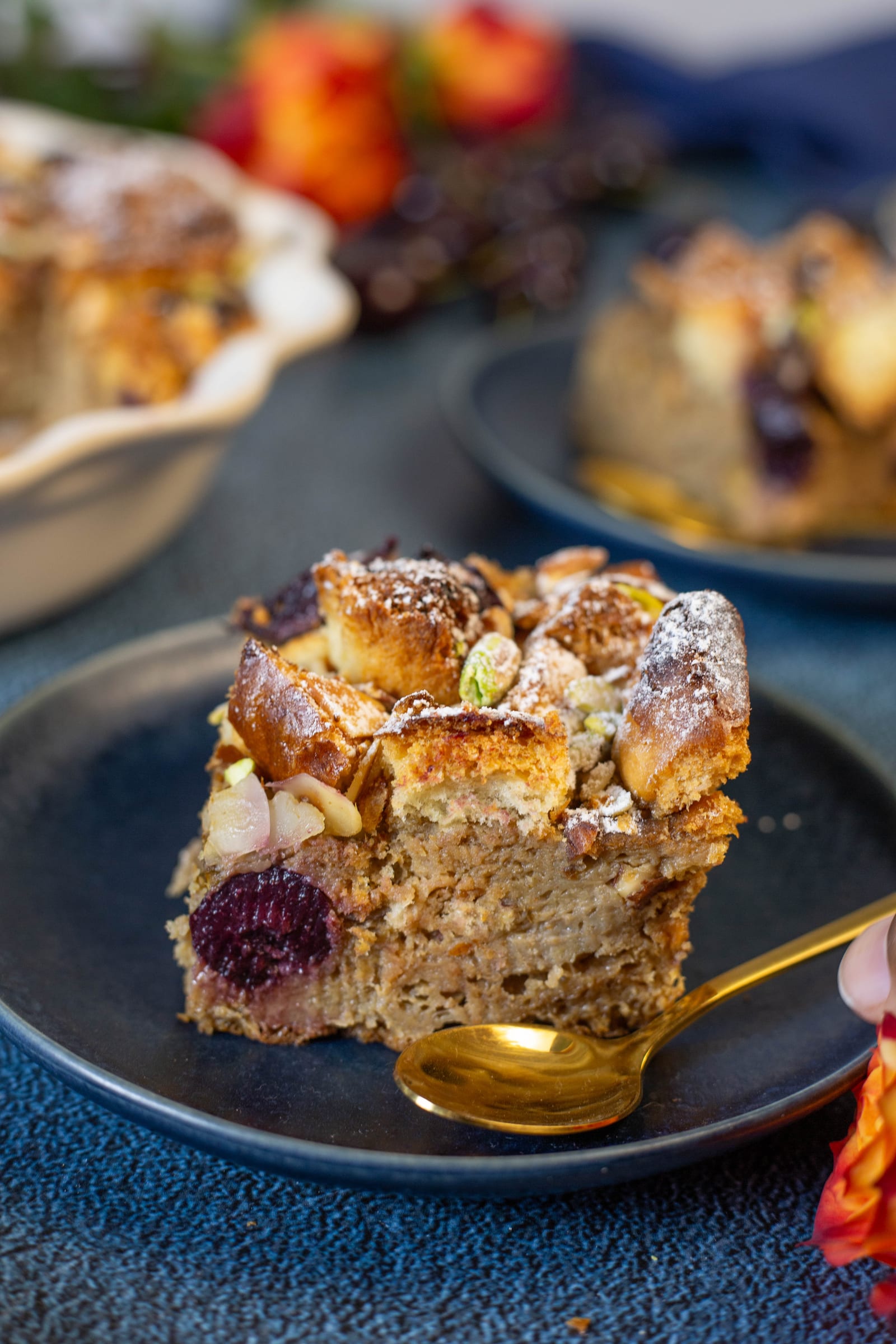 A square of bread and butter pudding on a dark plate with a gold spoon