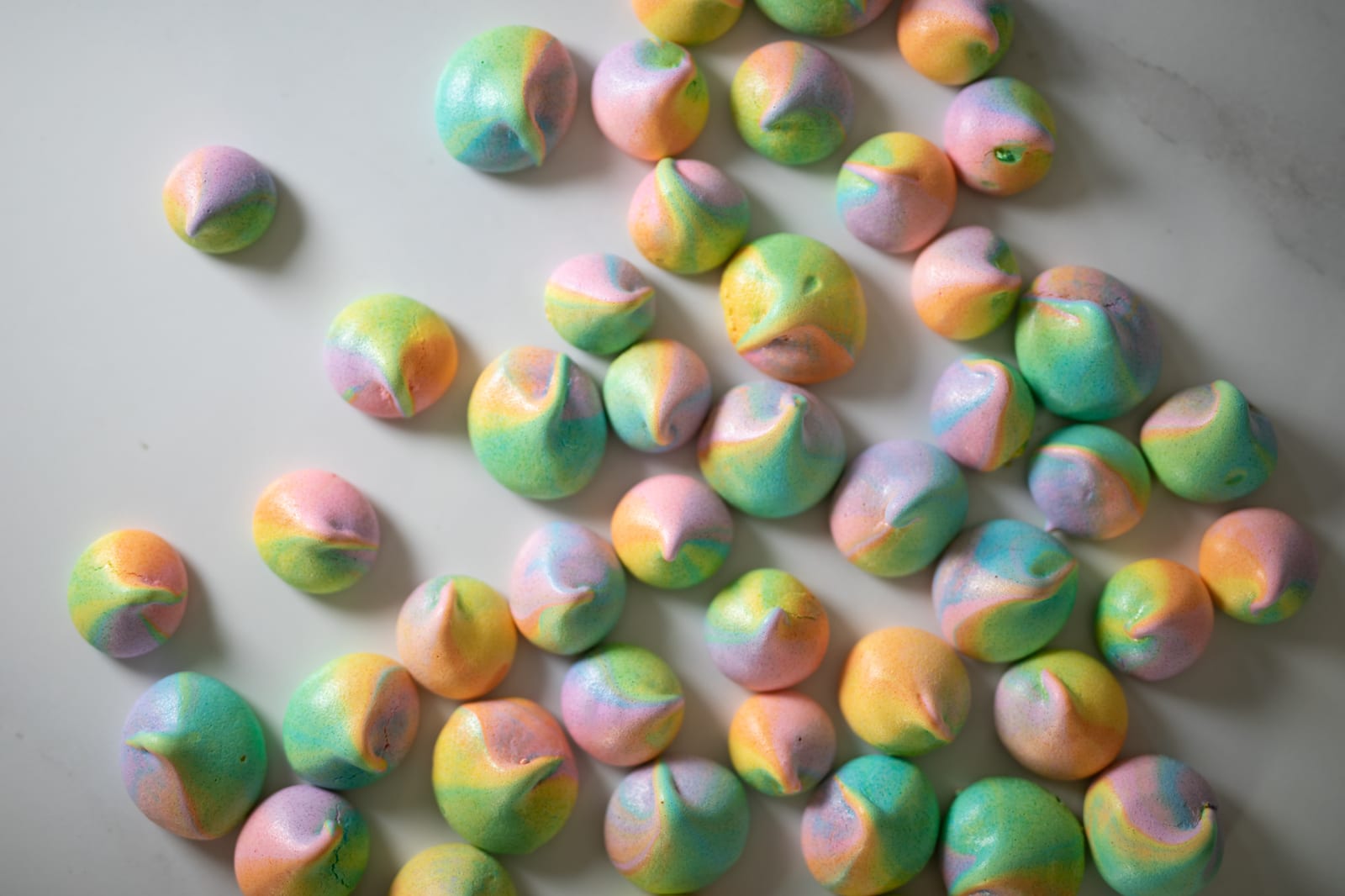 Rainbow meringue kisses scattered on a white surface, from above