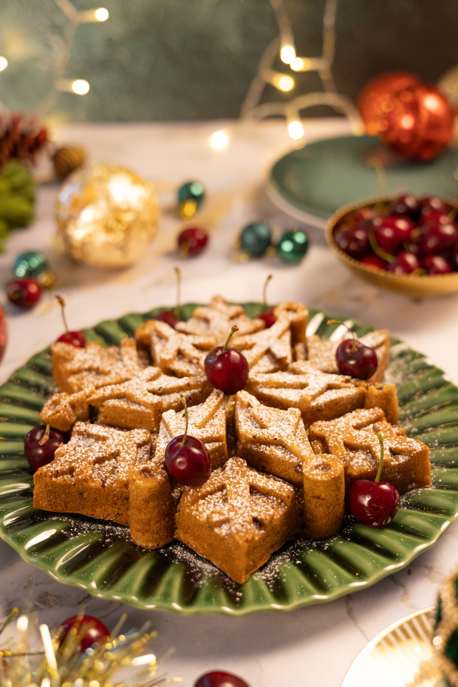 The snowflake fruitcake on a green plate, with fairy lights and cherries behind