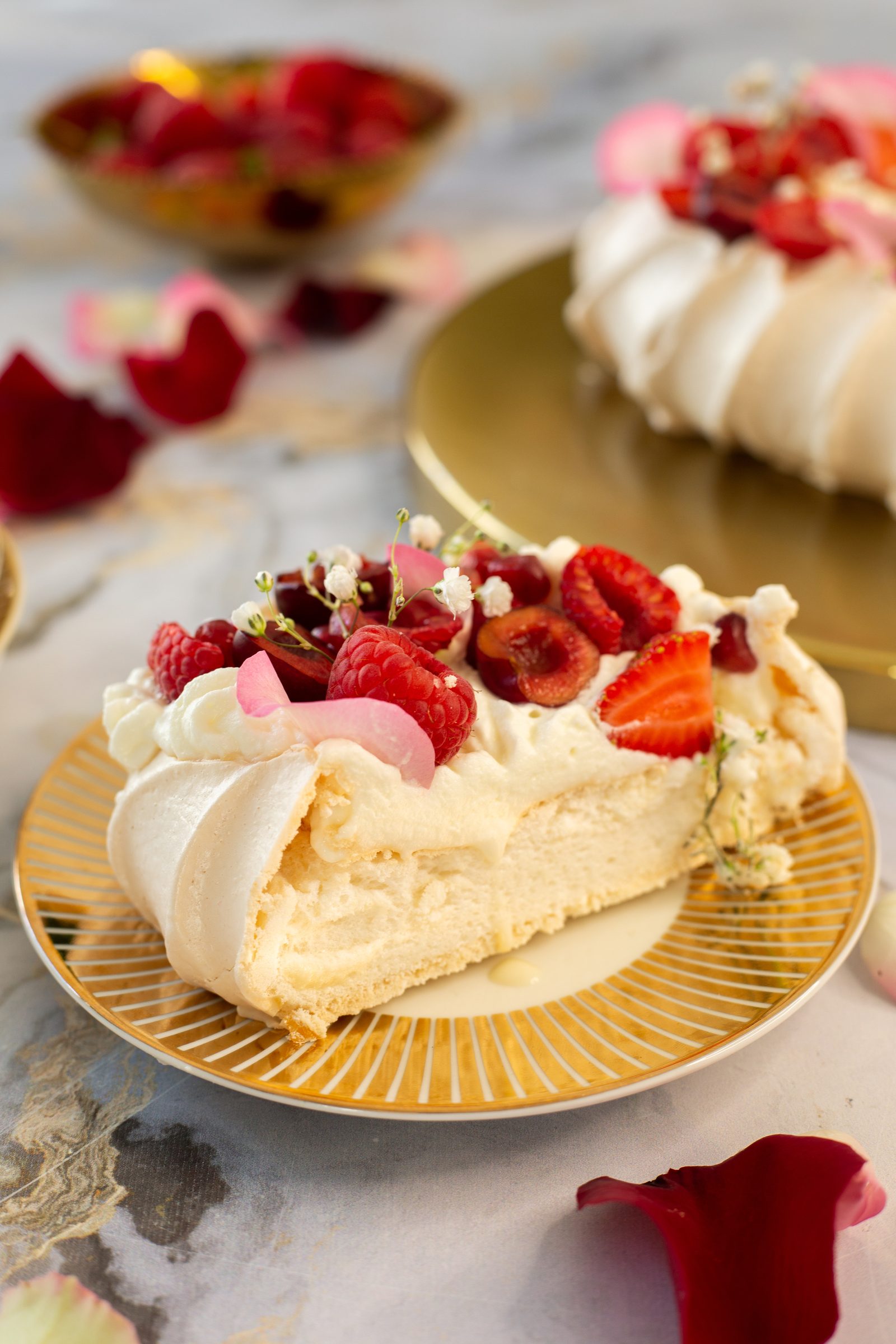 A slice of berry pavlova on a gold-rimmed plate showing its soft marshmallowy middle, from the side