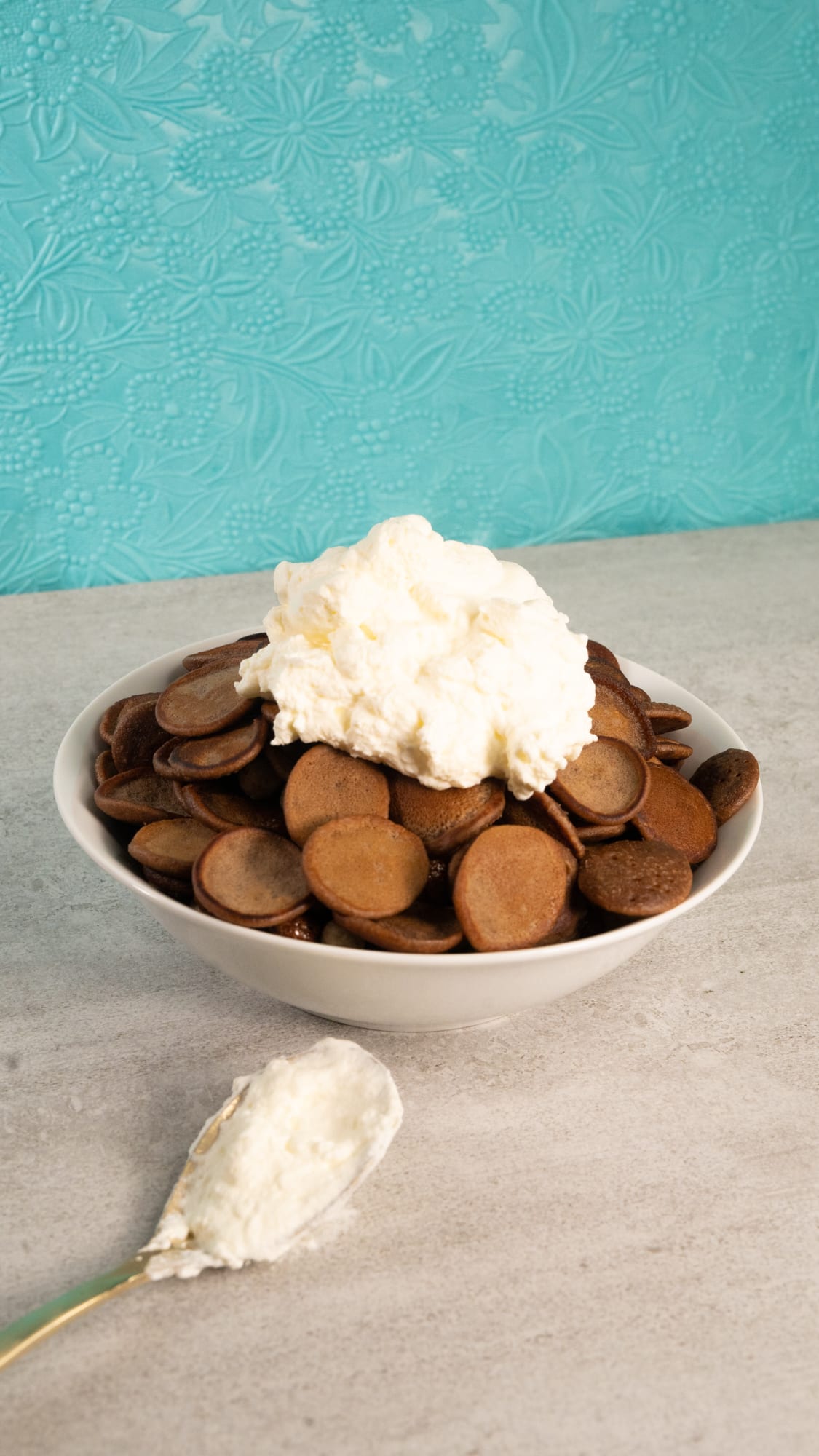 A bowl of Milo pancake cereal topped with cream against a turquoise wall