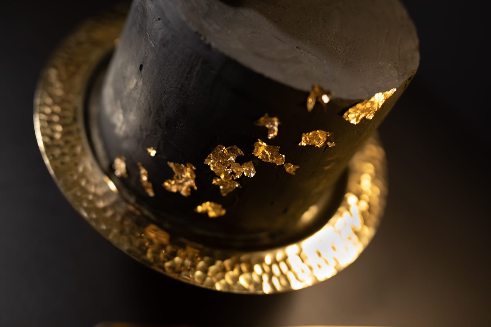 Close-up of the gold leaf on the side of a black velvet cake and the hammered gold rim of its stand