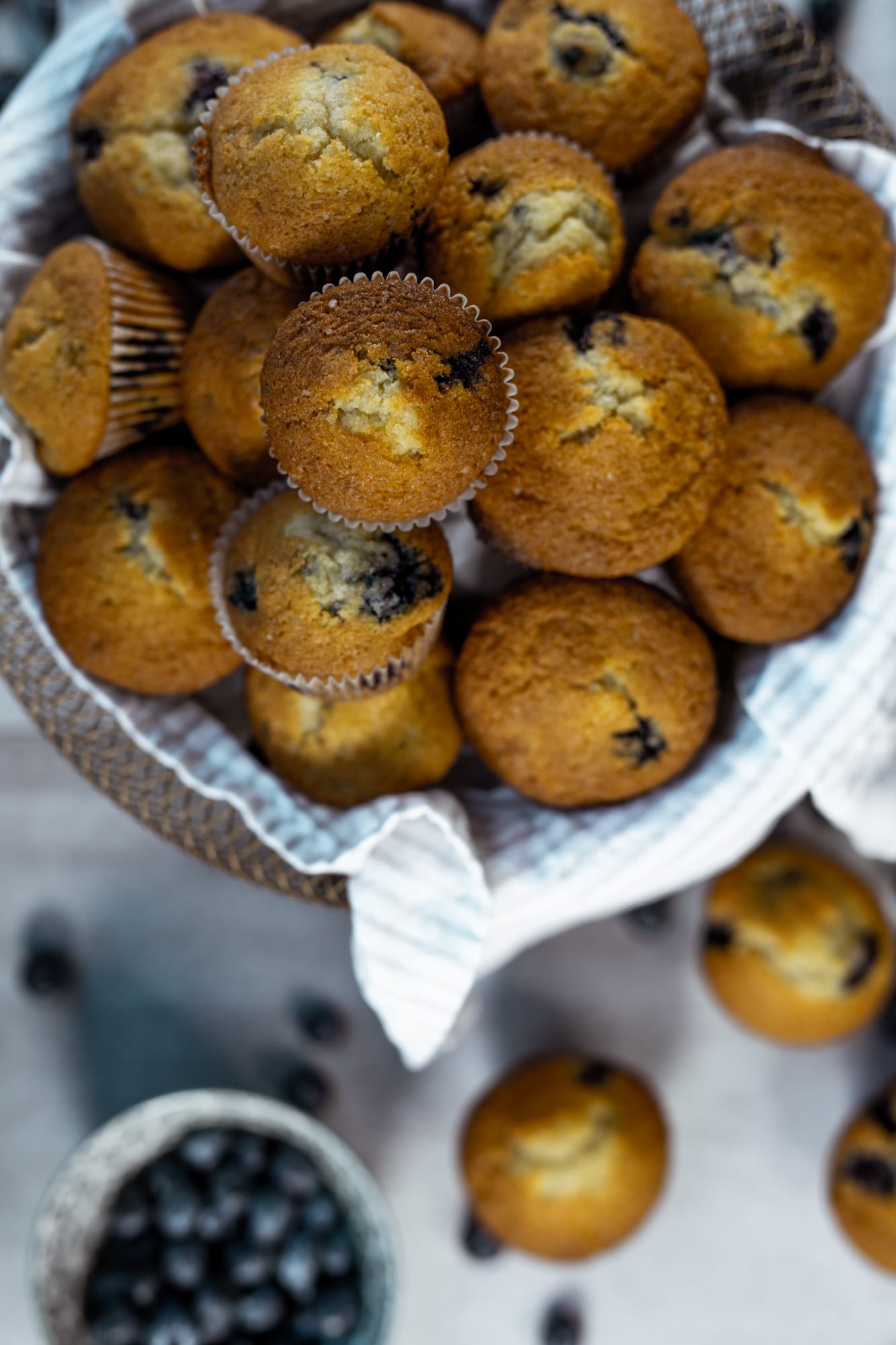 A gingham-lined basket piled with one bowl blueberry muffins, from above