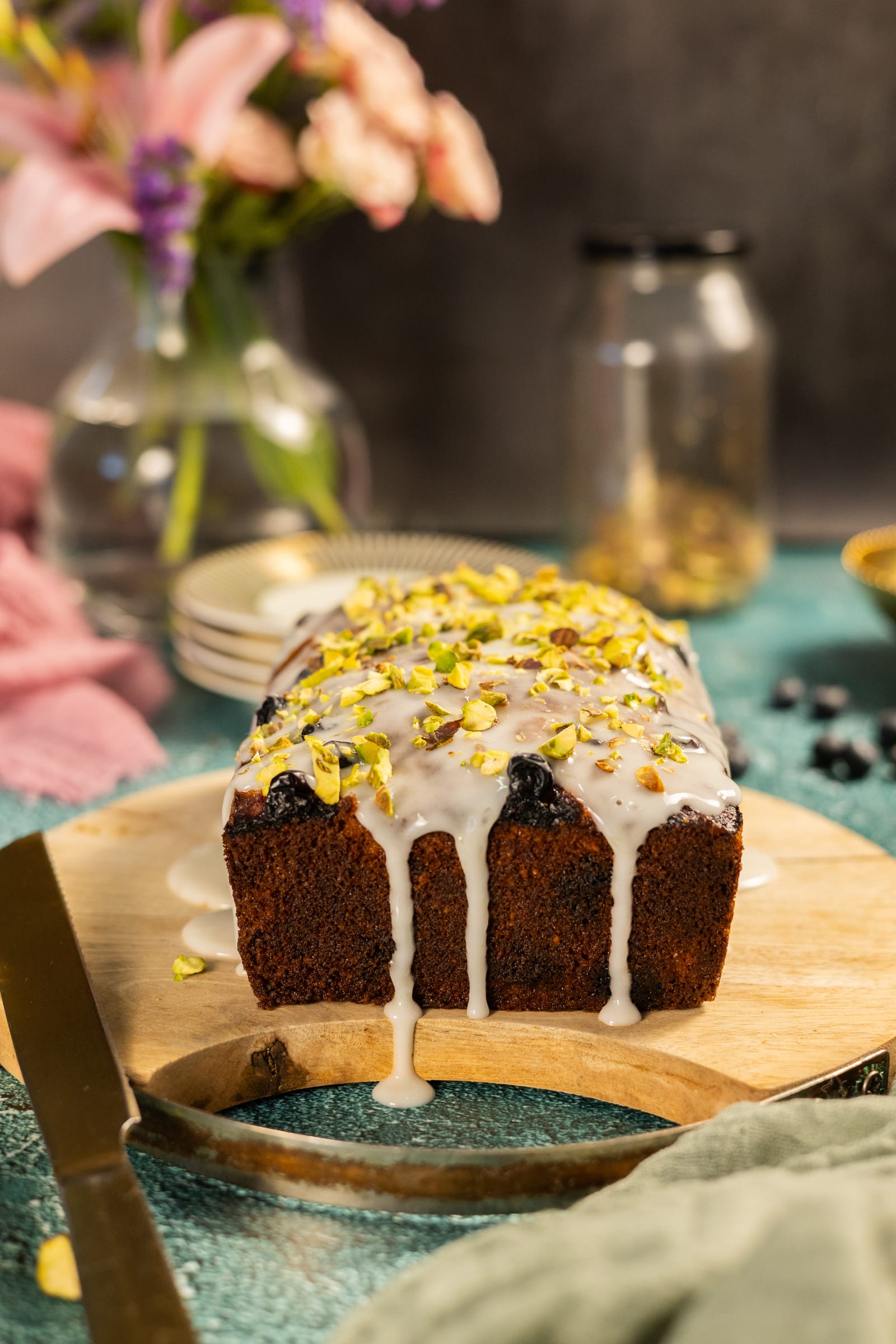 The glazed loaf topped with chopped pistachios, with pink flowers behind