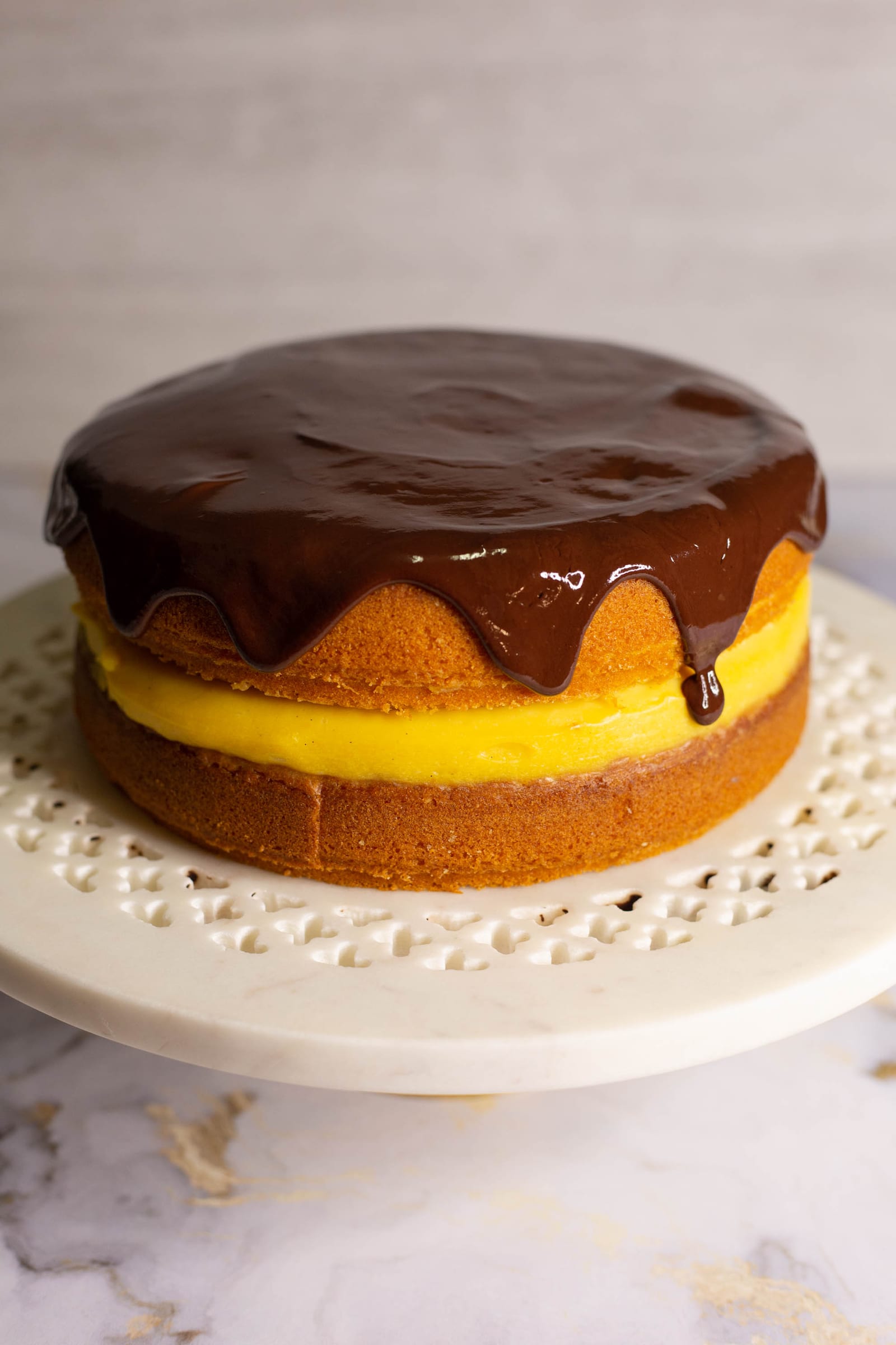 A whole Boston cream pie on a cake stand with ganache dripping down the sides