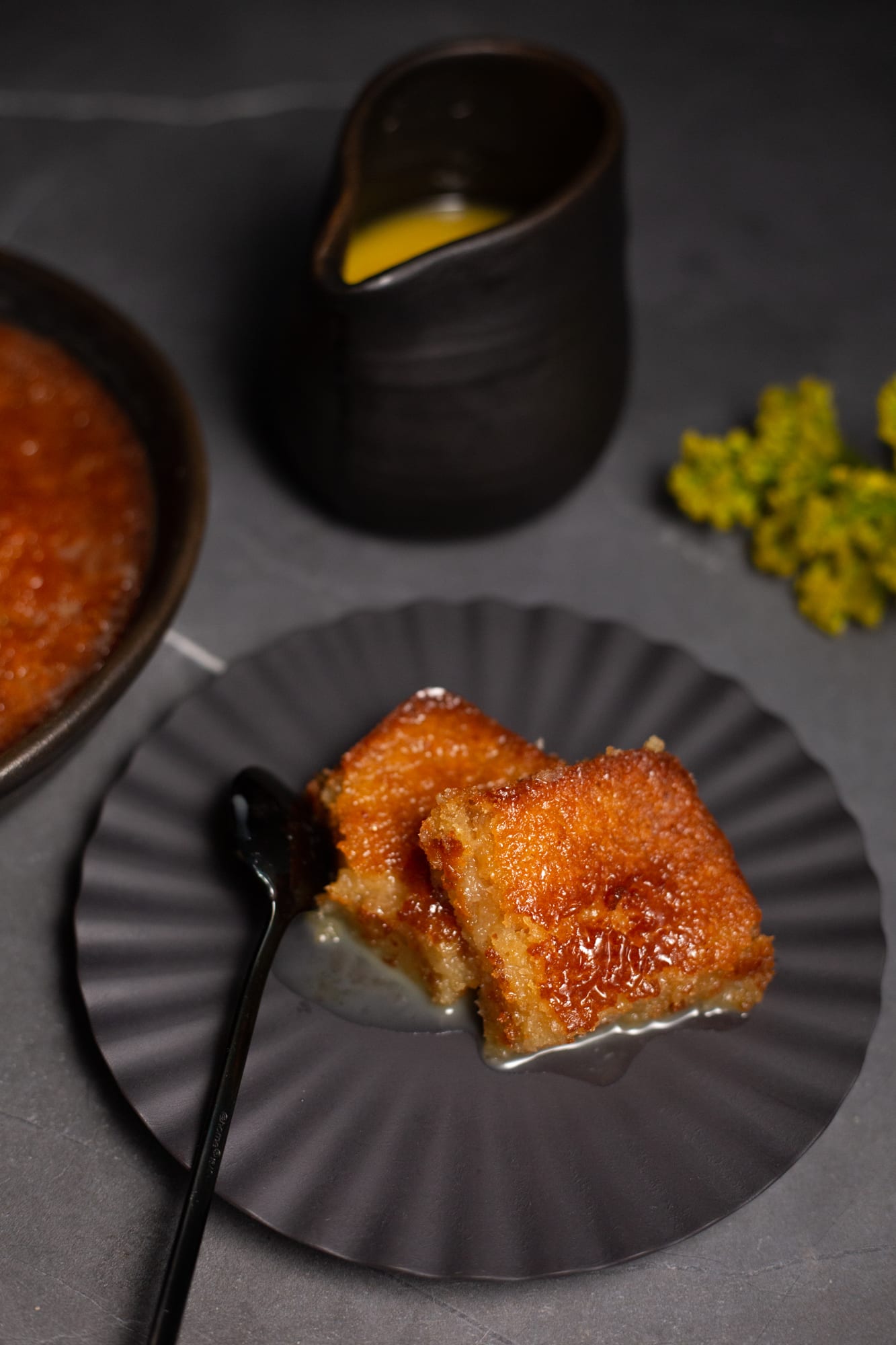 Squares of malva pudding on a plate, with a jug of custard