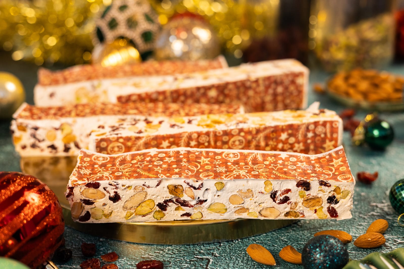 Bars of cranberry, pistachio and almond nougat stacked on a gold plate, with Christmas baubles