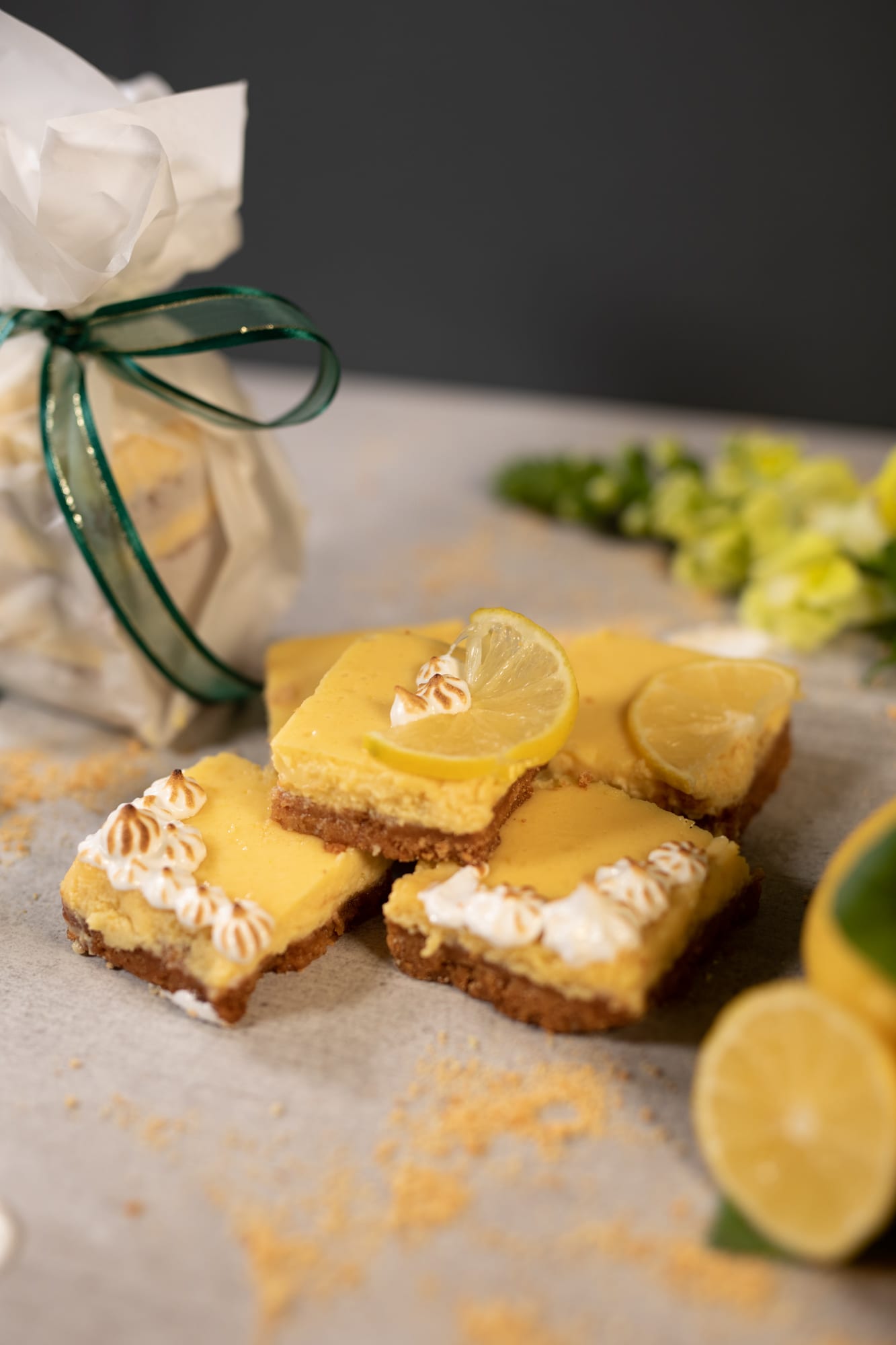 Stacked sweet and tart lemon squares in front of a gift bag tied with green ribbon