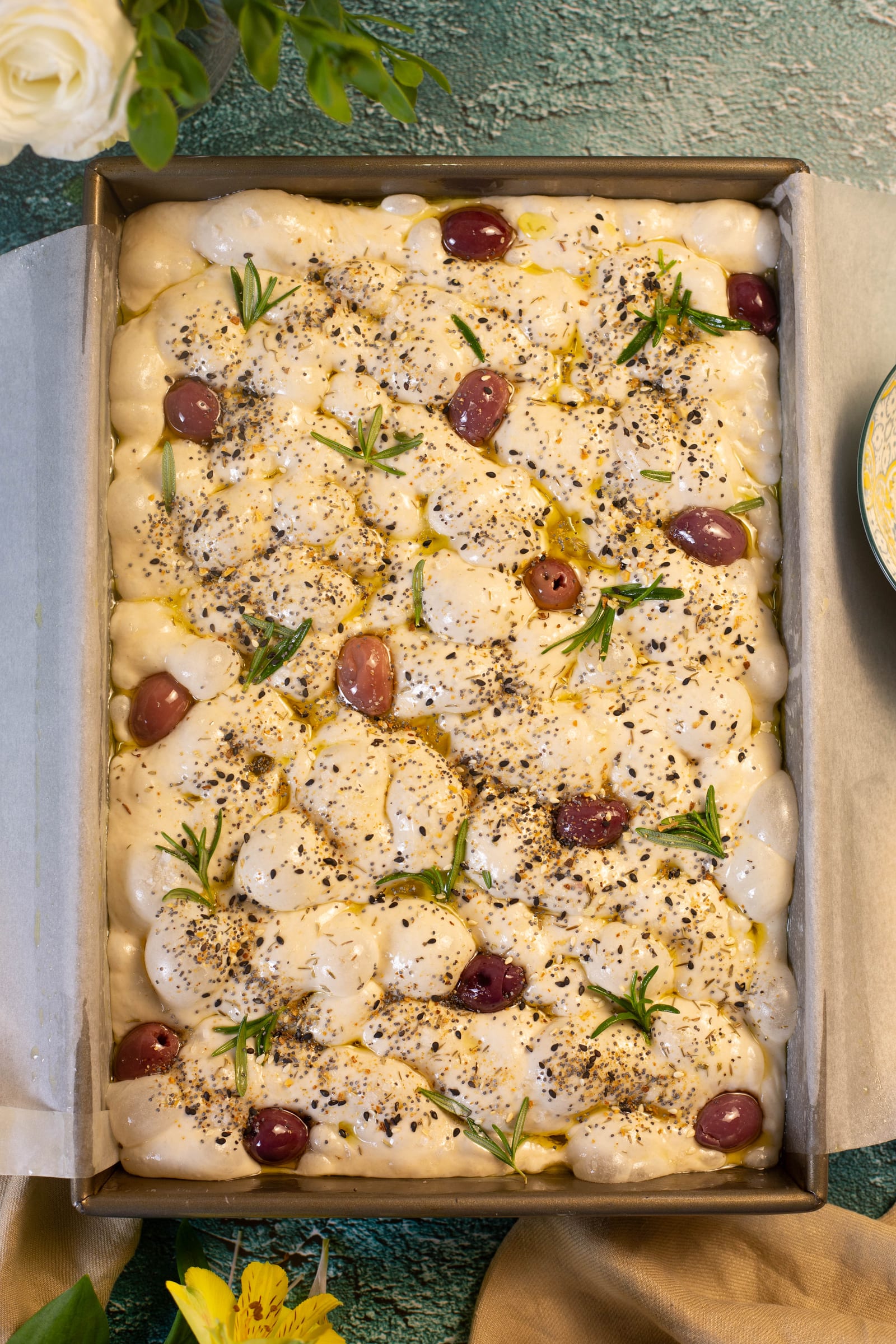 Focaccia dough dimpled with olives and rosemary, before baking
