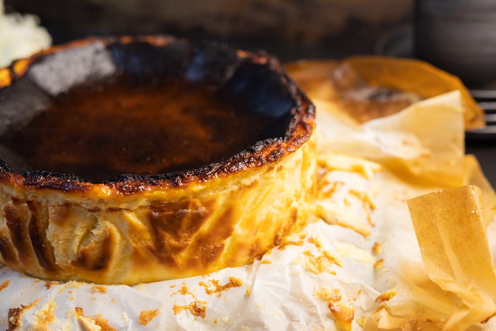 A whole Basque cheesecake from the side, its scorched sides rising out of crinkled baking paper