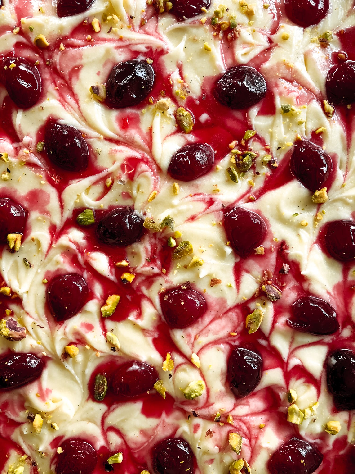 Close-up of the cherry swirl and pistachios on top of a pistachio and cherry sheet cake, from above