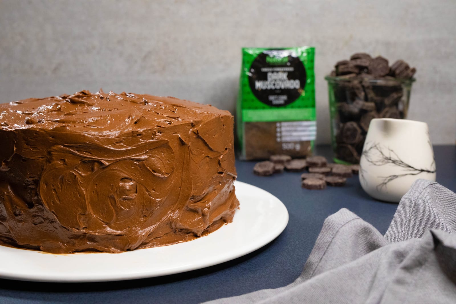 A whole chocolate fudge cake with a pack of Natura Sugars dark muscovado sugar and chocolate behind
