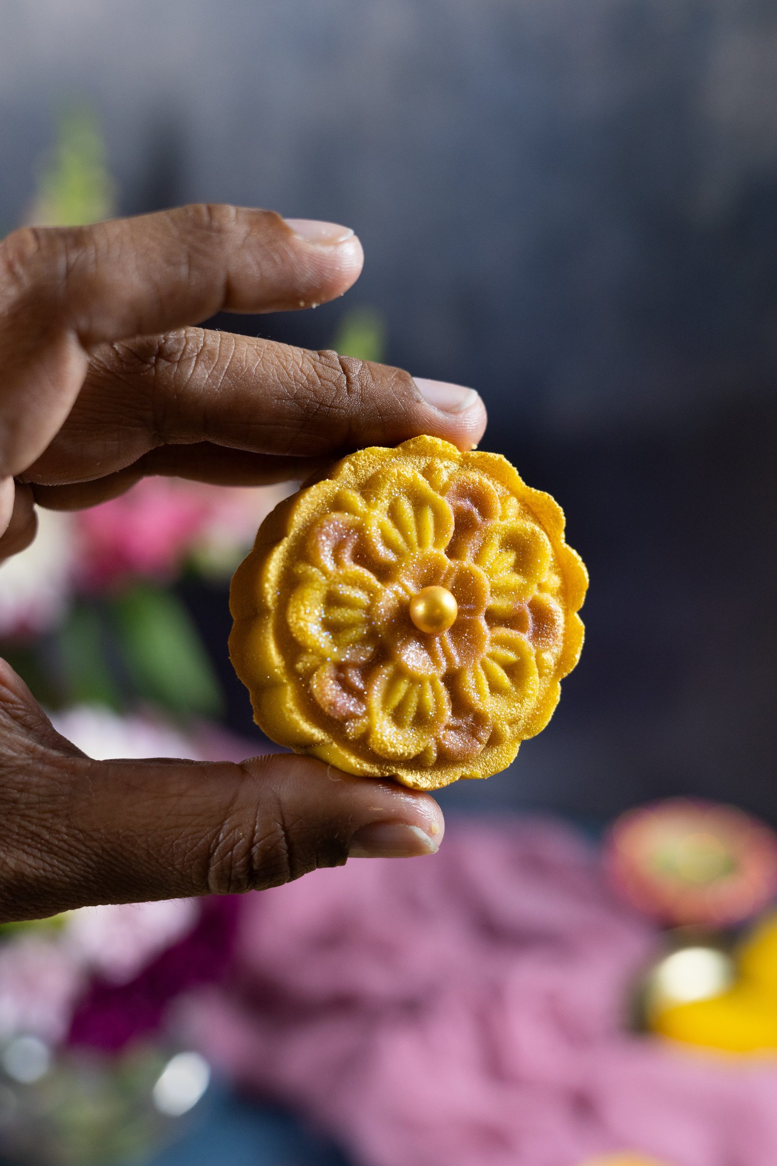 A hand holding up a single flower-shaped mango burfee