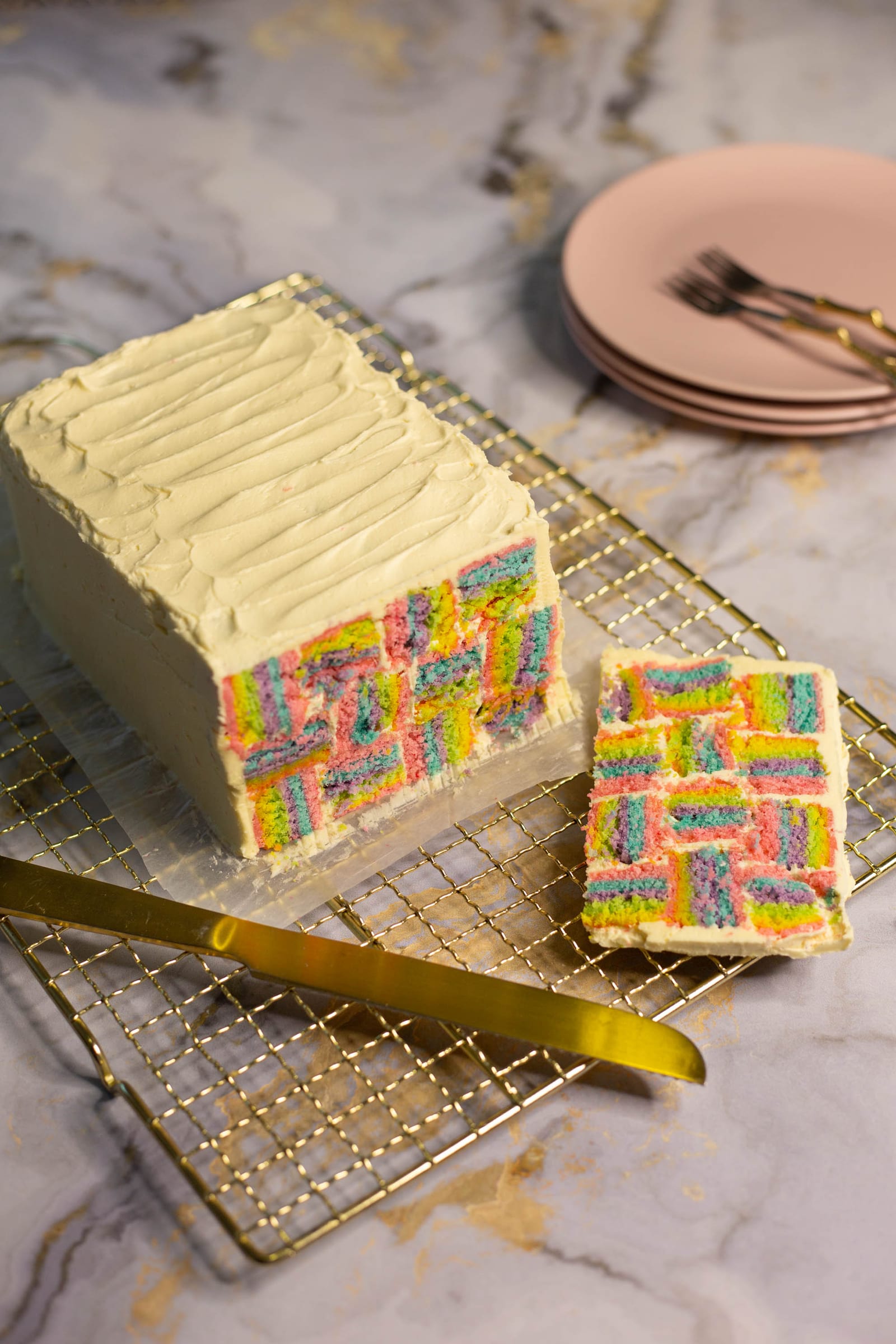 A rainbow coconut layer cake with its end cut off and a slice beside it, a gold knife in front