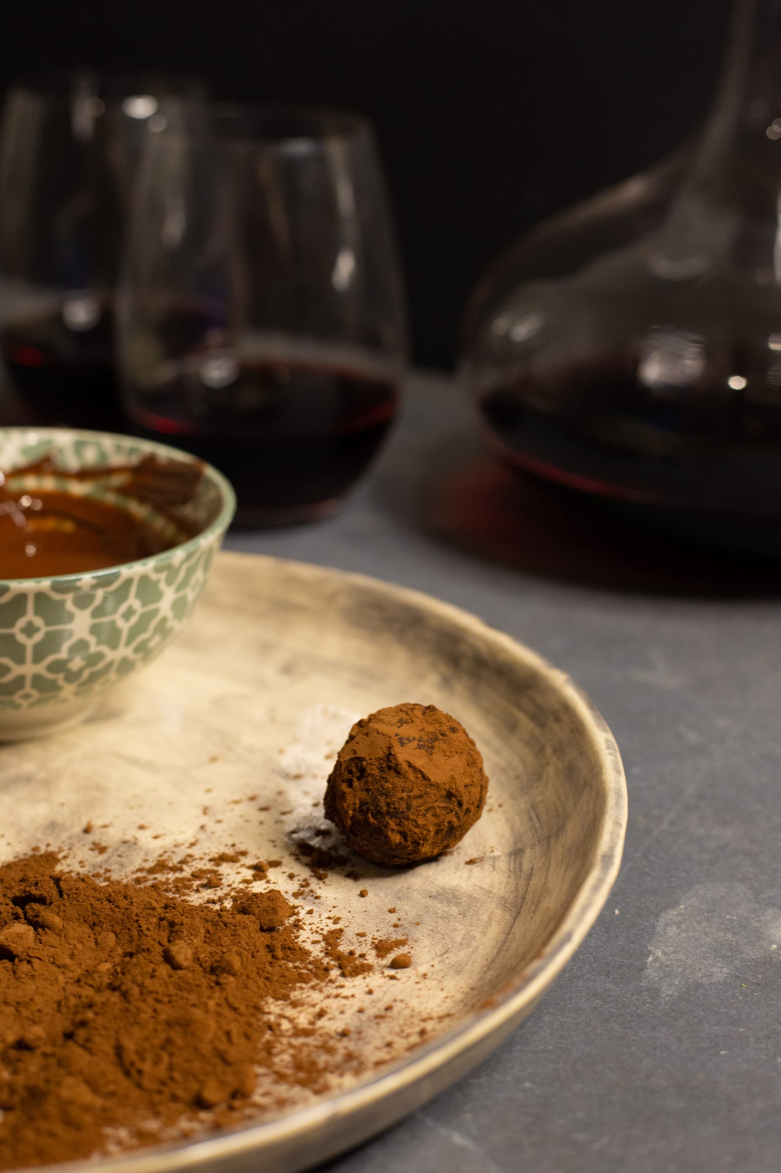 A rum and raisin truffle in cocoa powder beside a bowl of melted chocolate, from slightly above