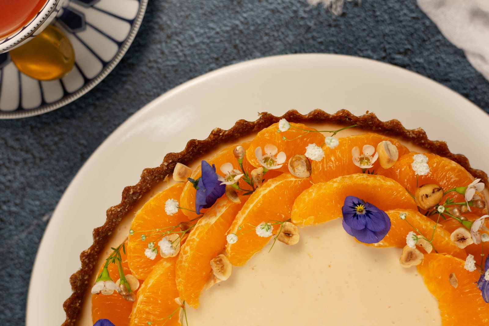 A rooibos panna cotta tart edged with clemengold segments, edible violets and hazelnuts