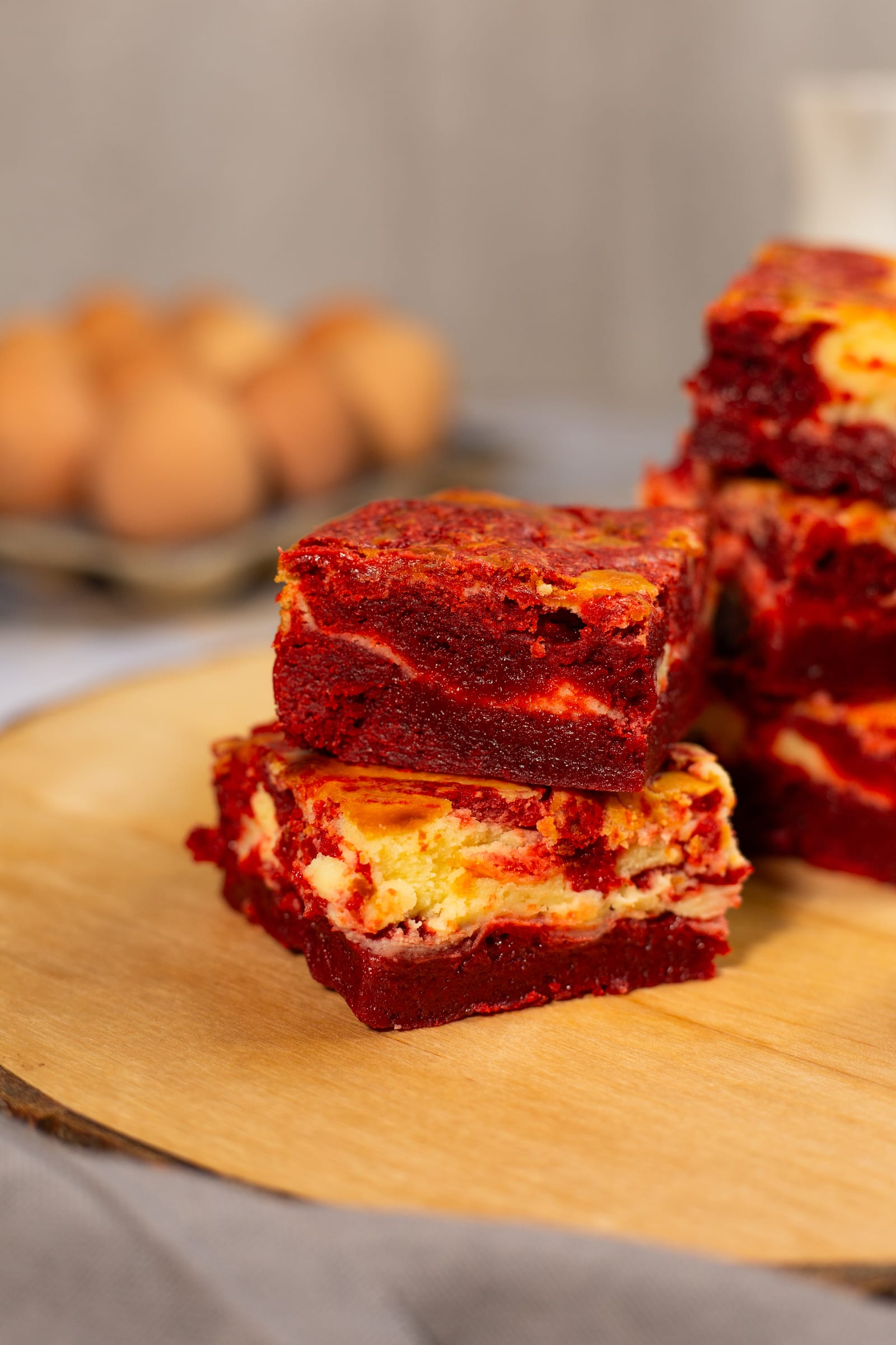 Two squares of red velvet cheesecake blondies stacked close up, showing the red and cream layers