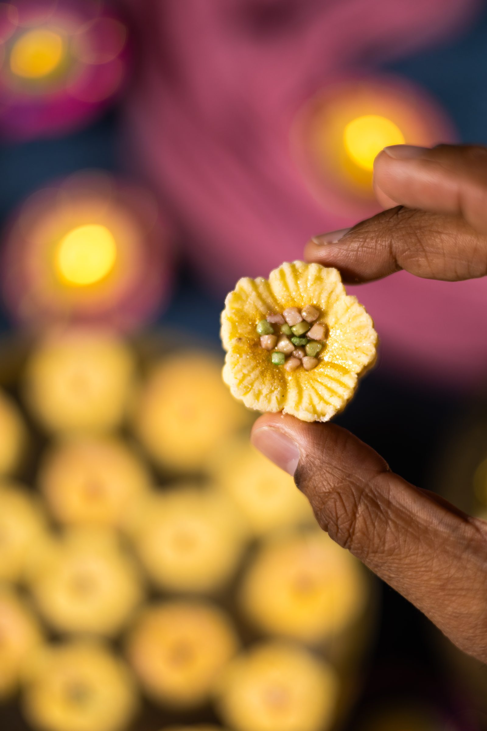 A single simply wonderful held up between two fingers in front of glowing diyas