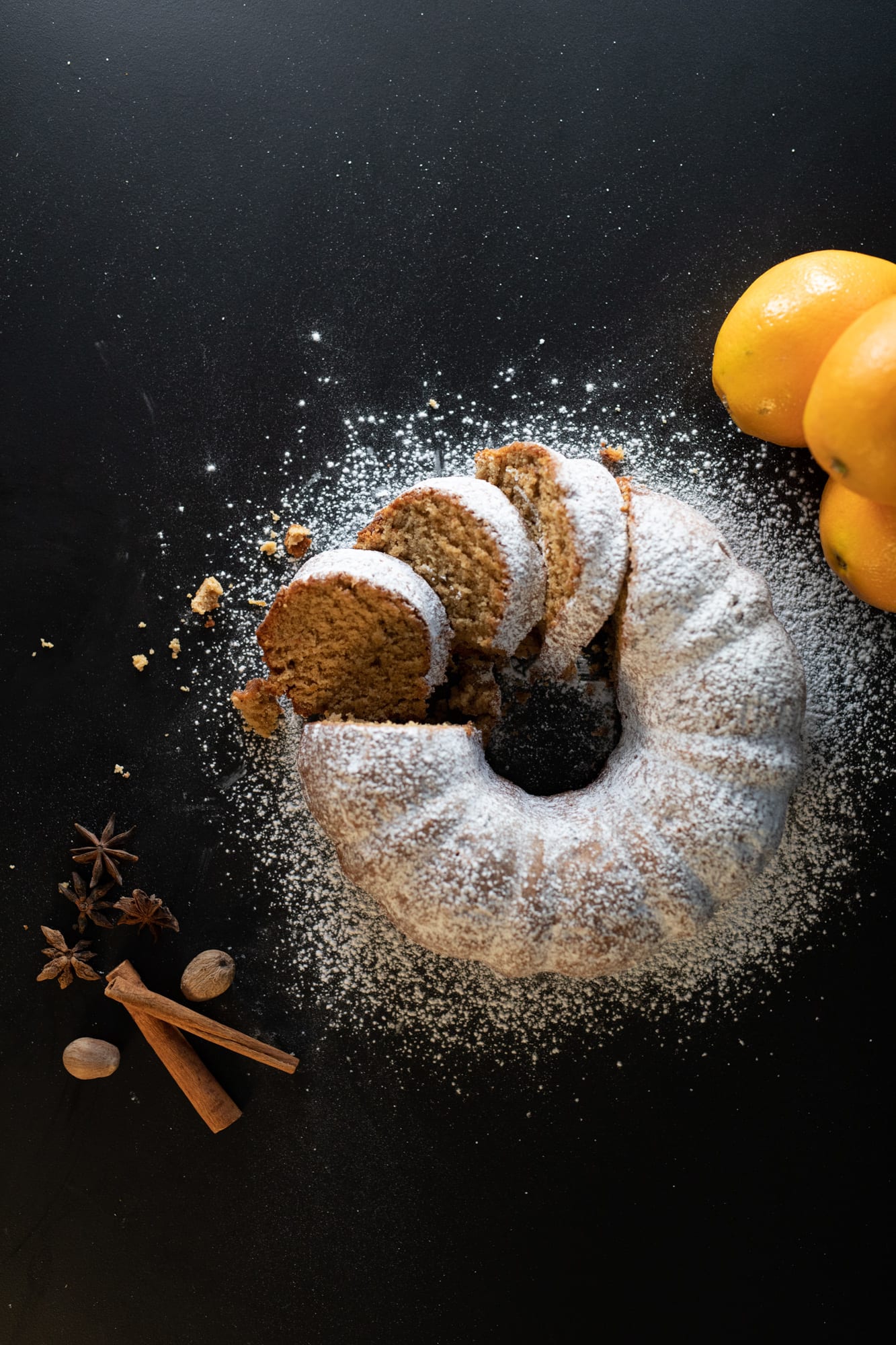 A sliced orange spice pound cake from above, with fanned slices beside oranges and spices