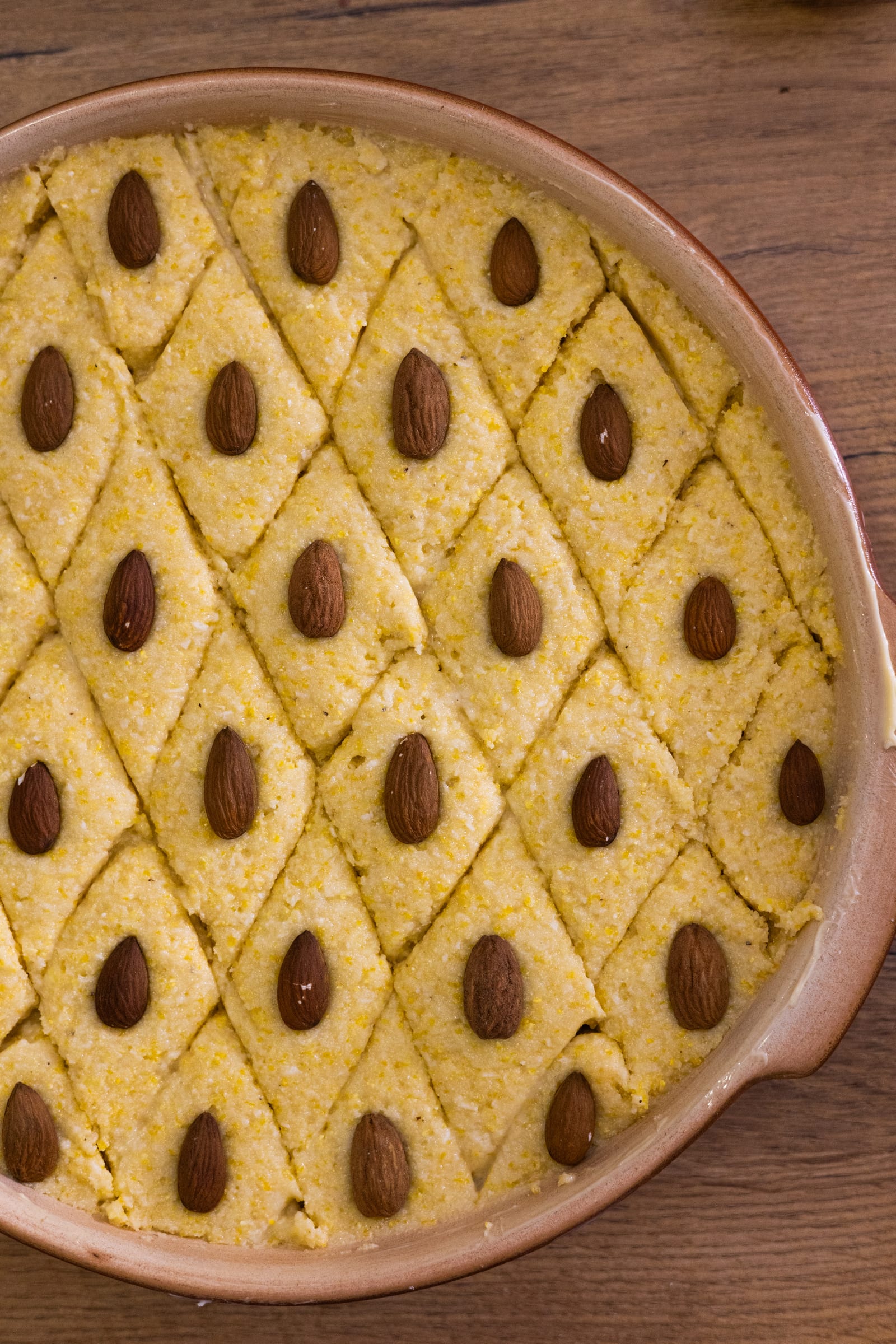 The unbaked basbousa scored into diamonds, each with an almond